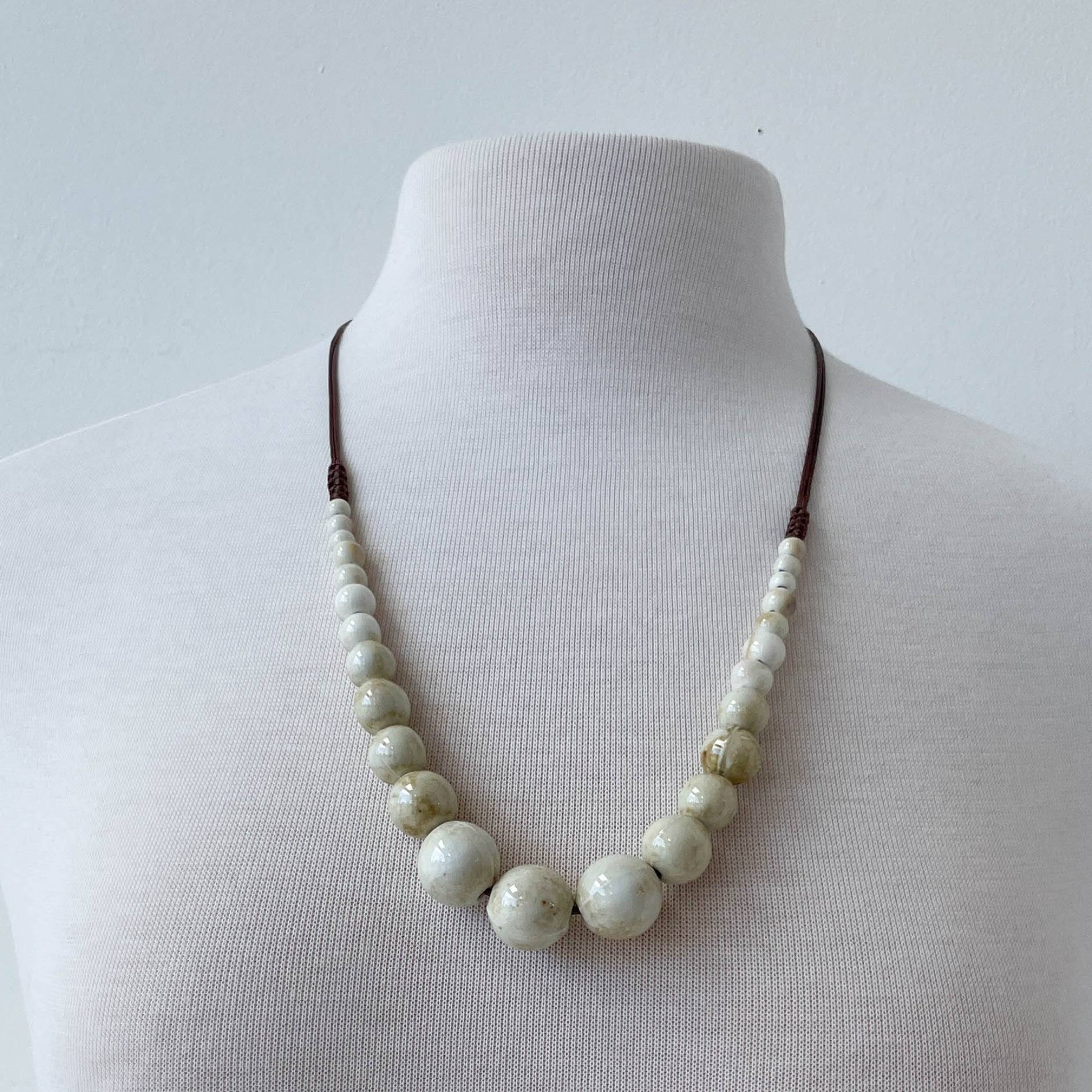 Ceramic necklace with large beads on a mannequin against a plain background