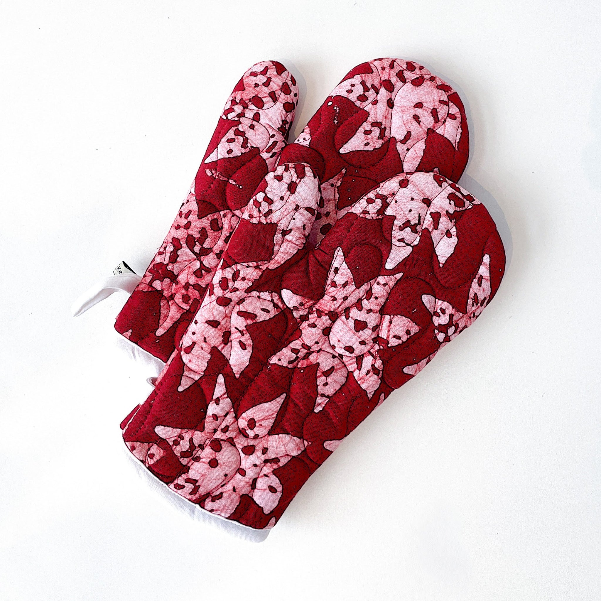 Pair of red and pink patterned oven mitts on a white background