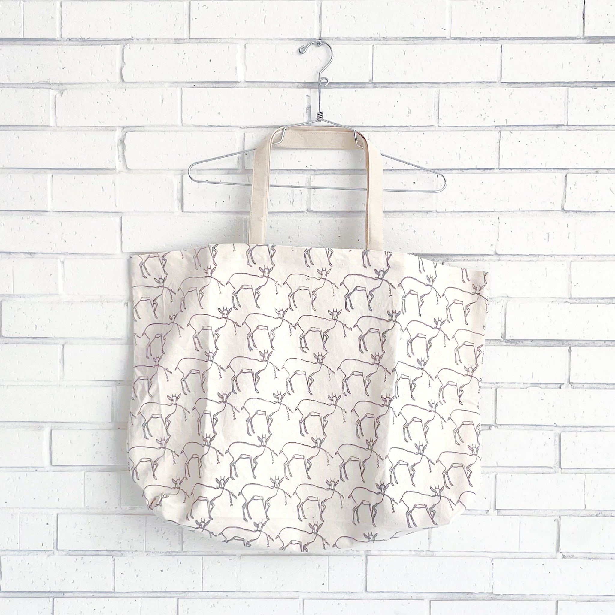 Tote bag with a pattern of small deer on a white brick wall background