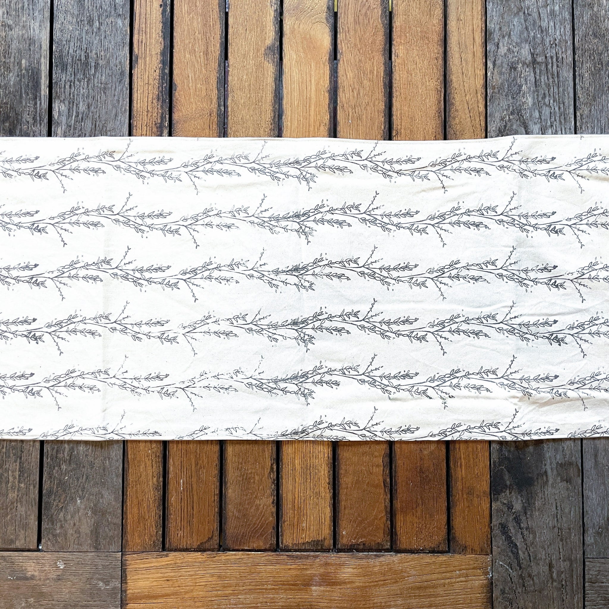 White table runner with grey floral pattern on a wooden surface