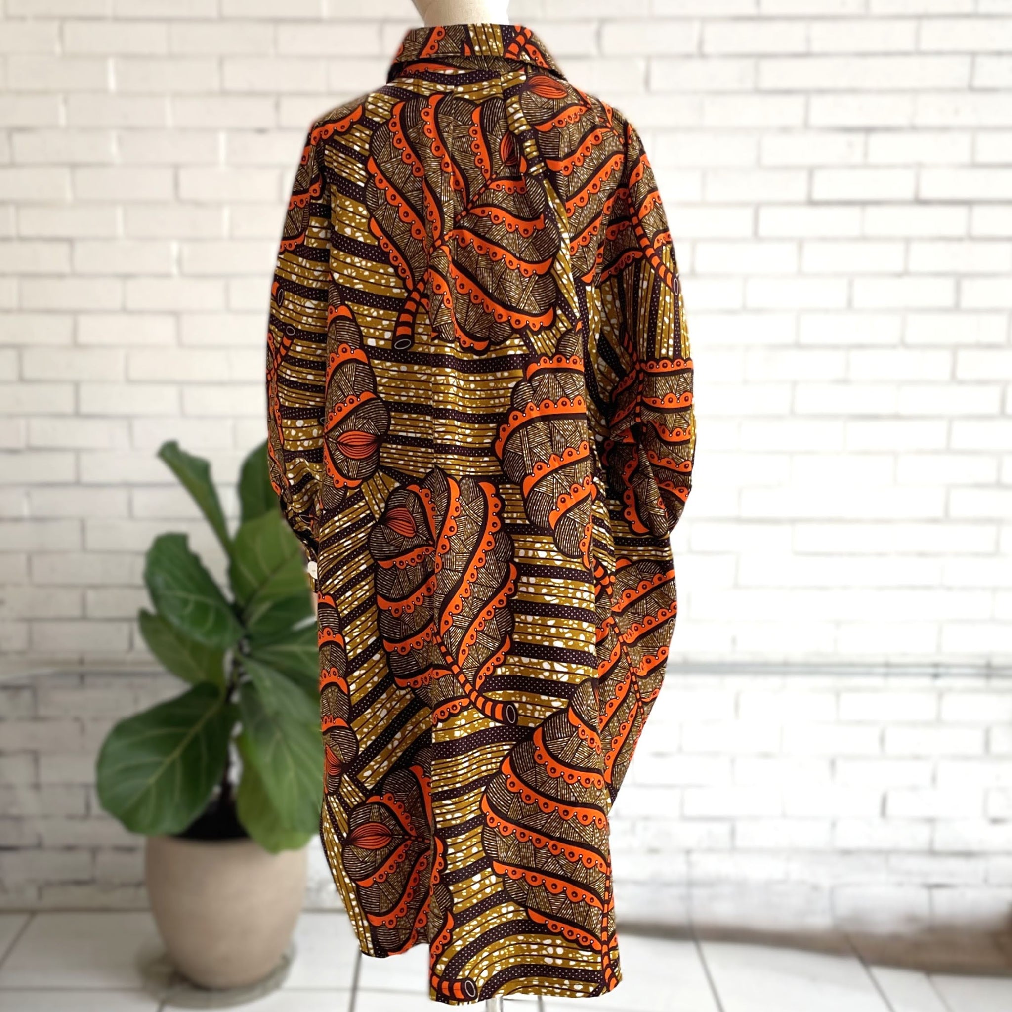 Mannequin wearing a patterned outfit with orange and gold design against a white brick wall.