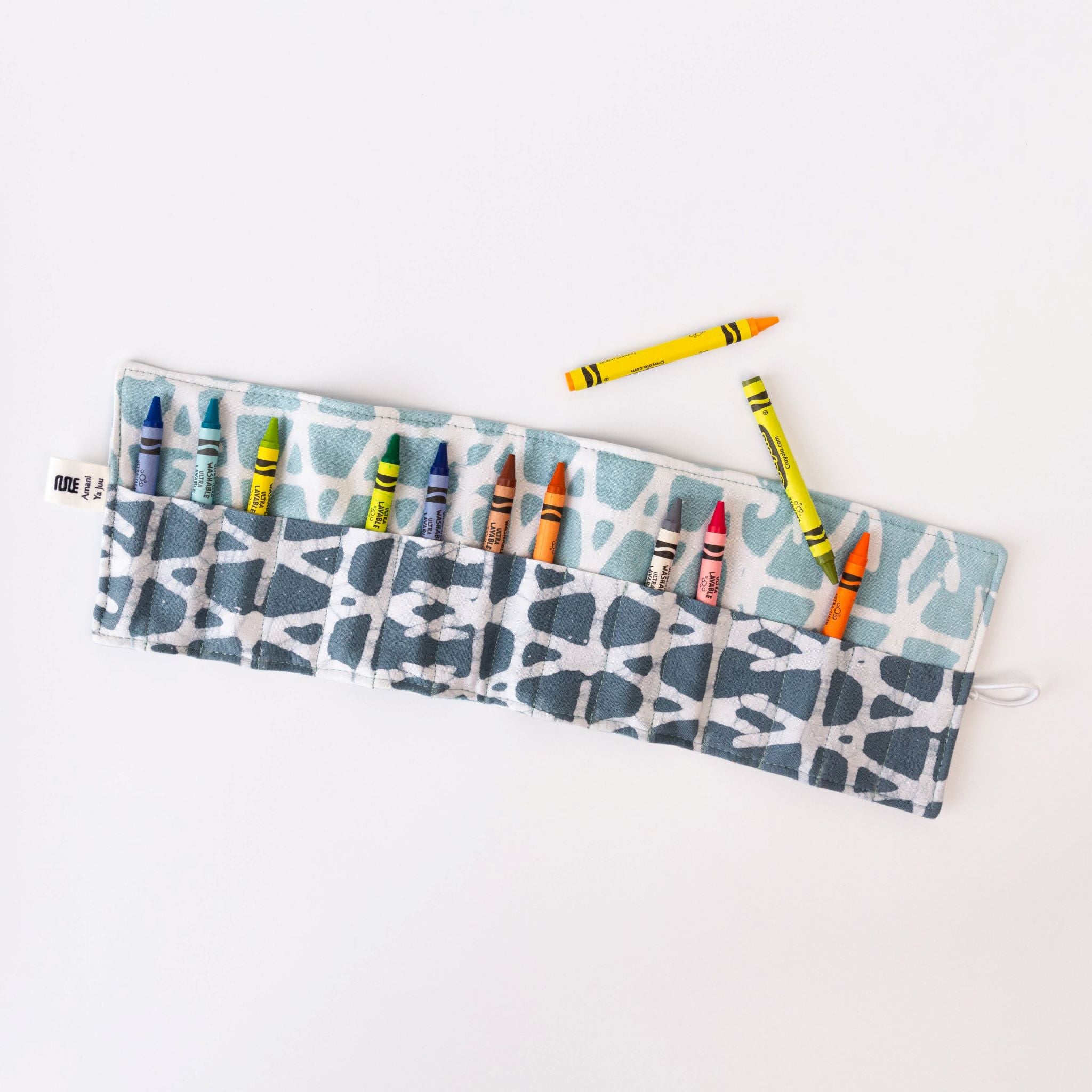 Fabric crayon holder pouch with crayons and tag on a light gray background