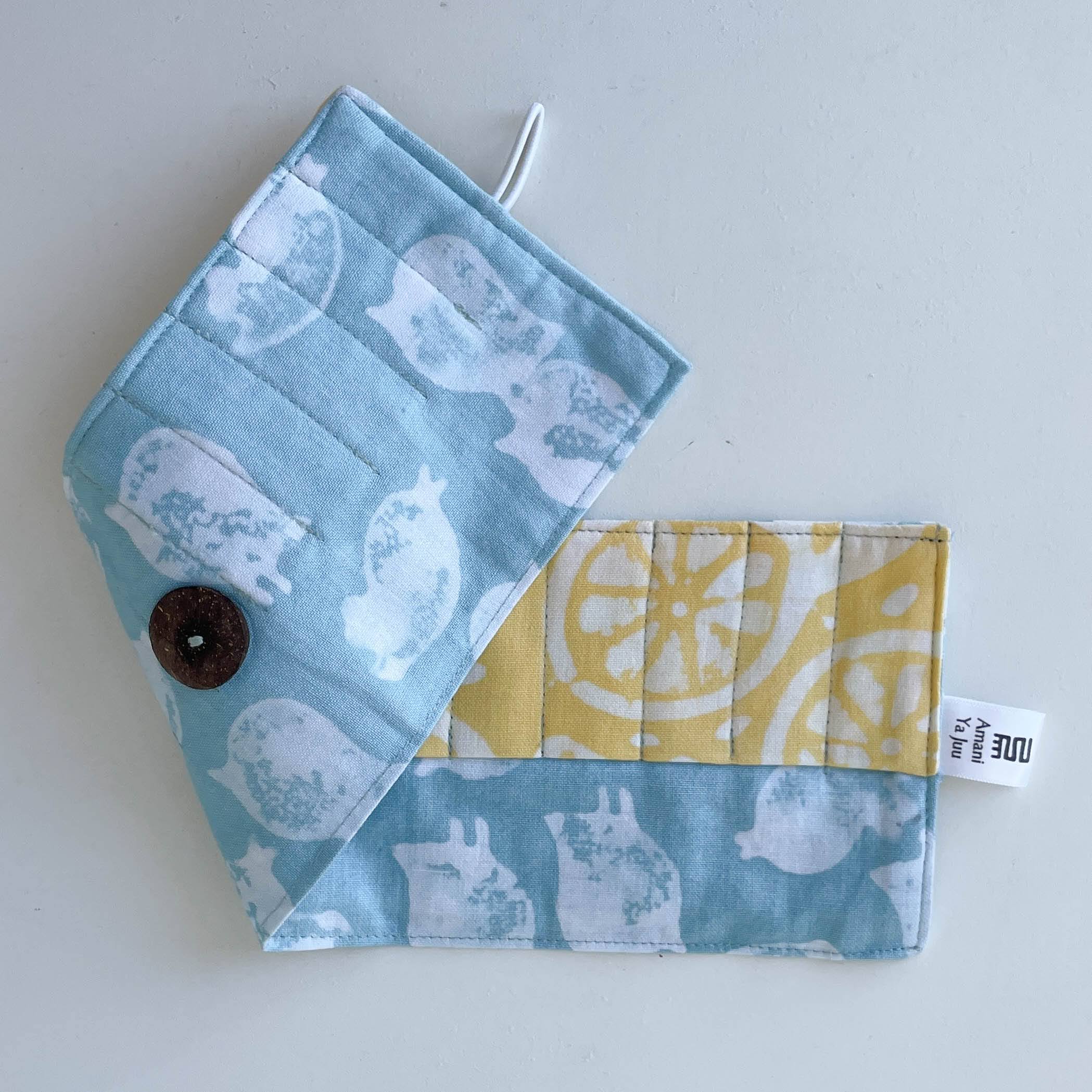 Fabric crayon holder pouch with button and tag on a light gray background