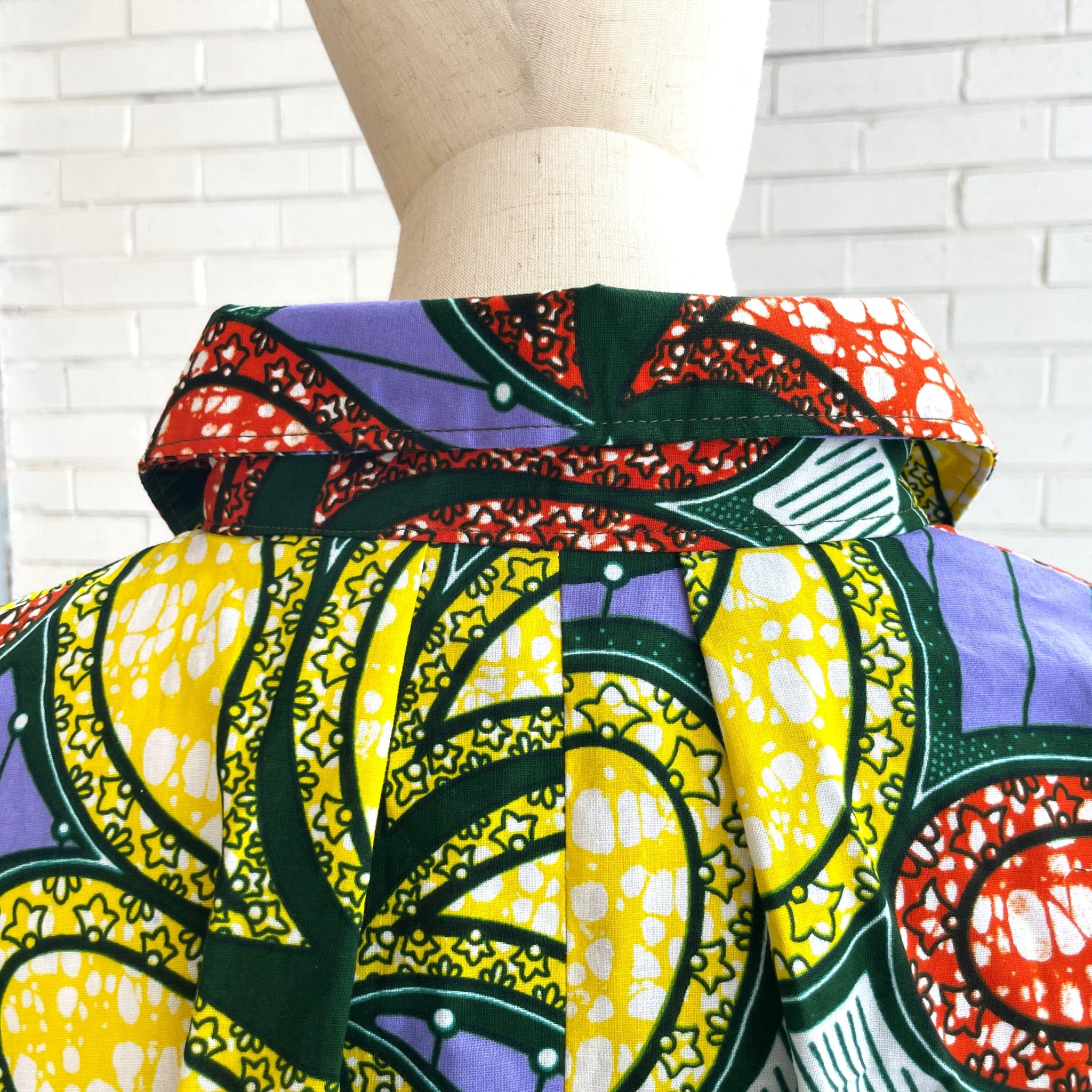 Colorful African print fabric on a mannequin against a white brick wall.