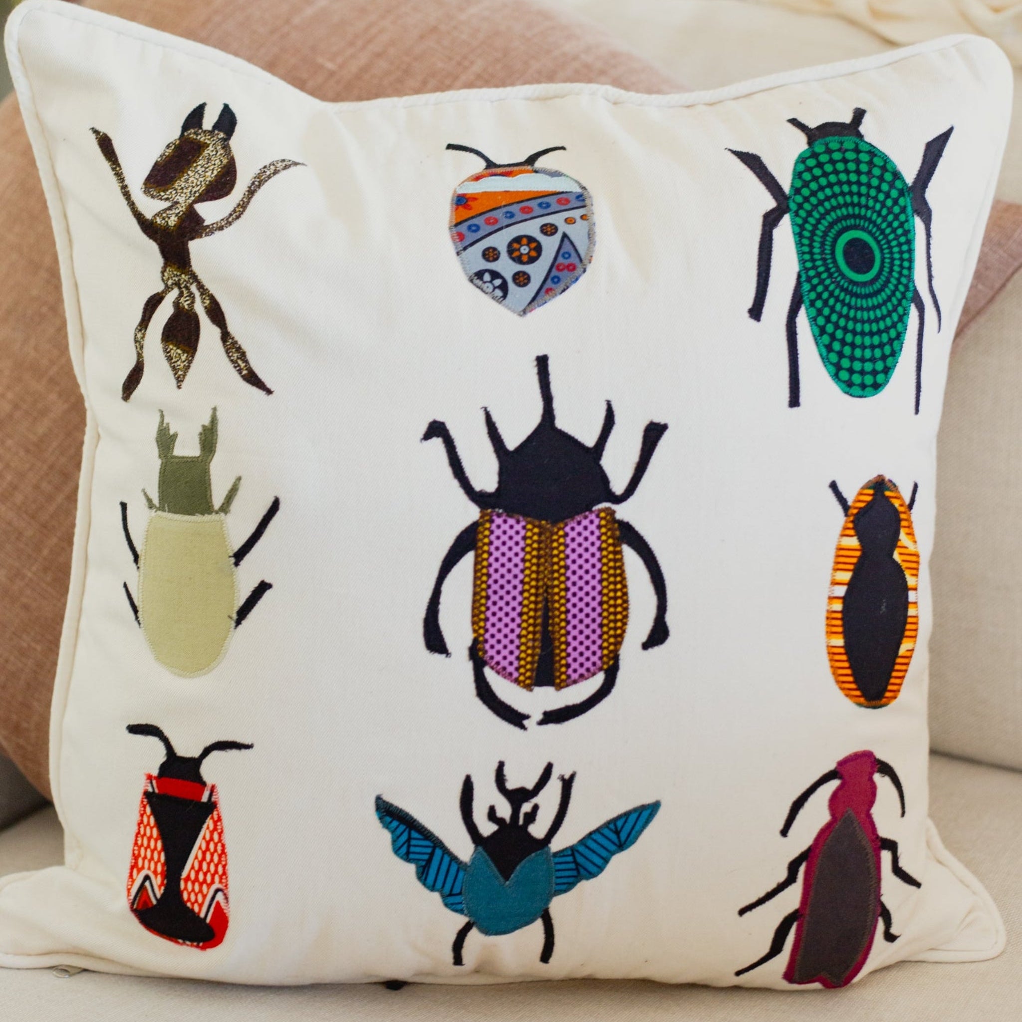 Decorative pillow with embroidered insect designs on a neutral background