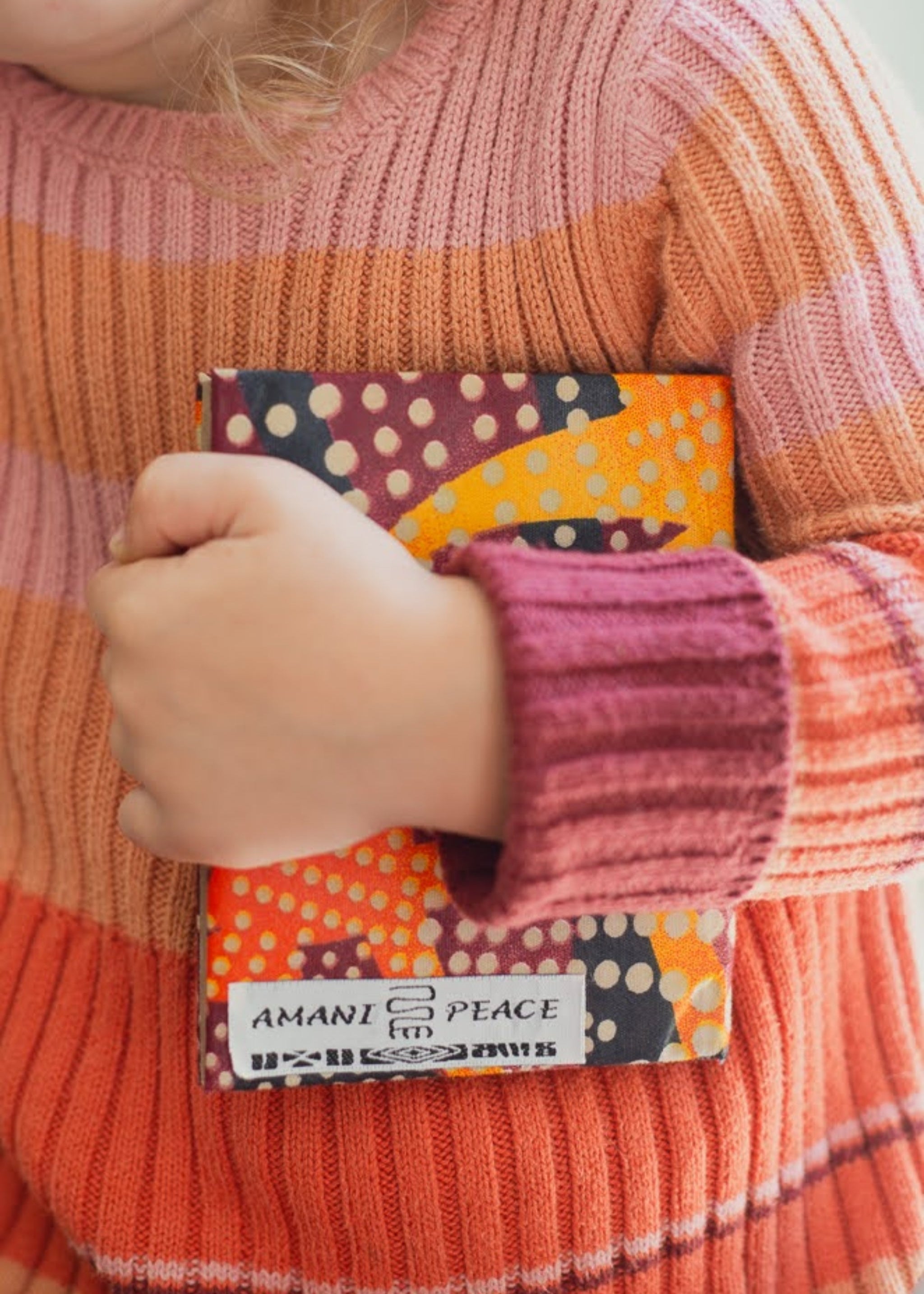 Child in striped sweater holding colorful cloth covered journal.