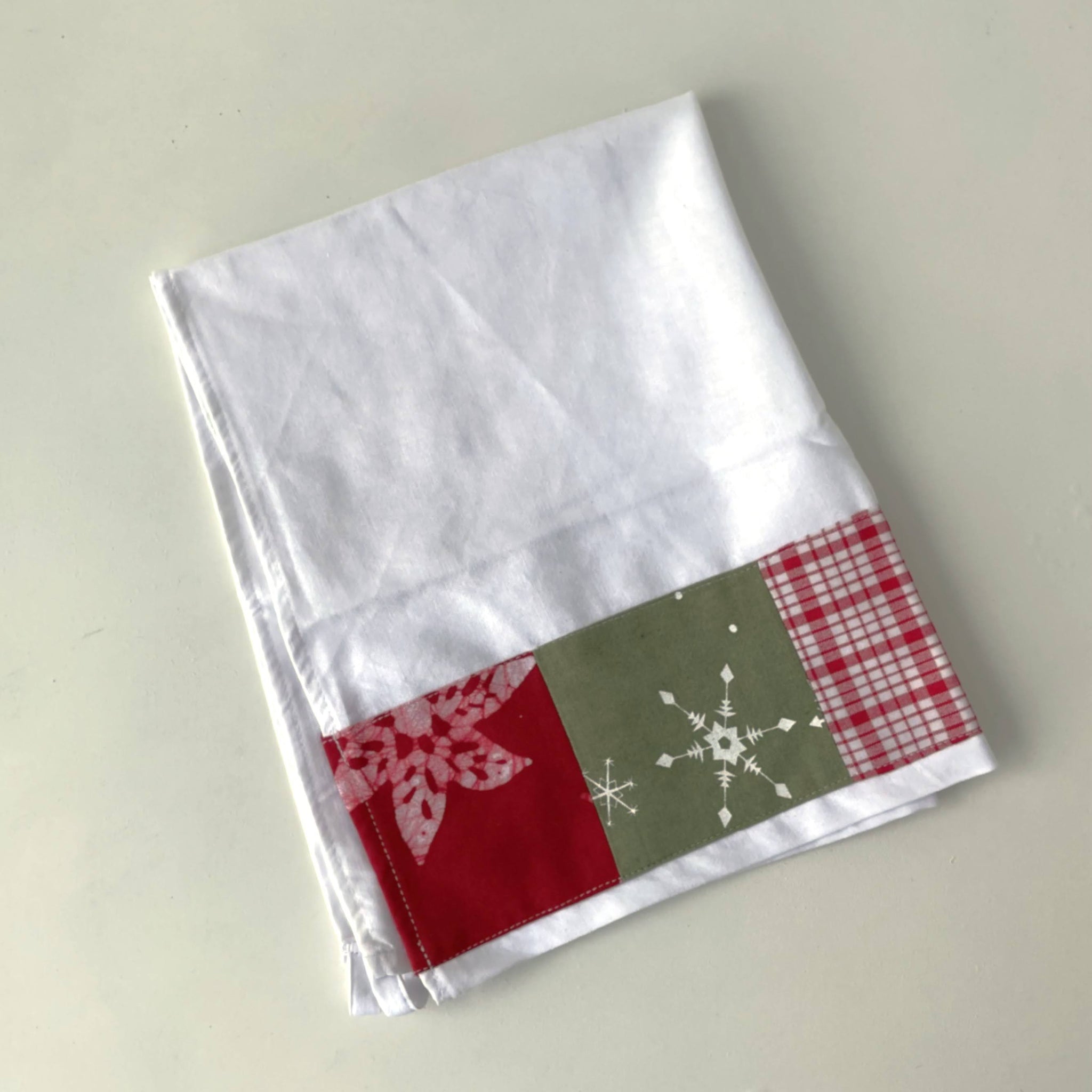 White fabric with red, green, and plaid border featuring snowflake patterns on a light gray background.