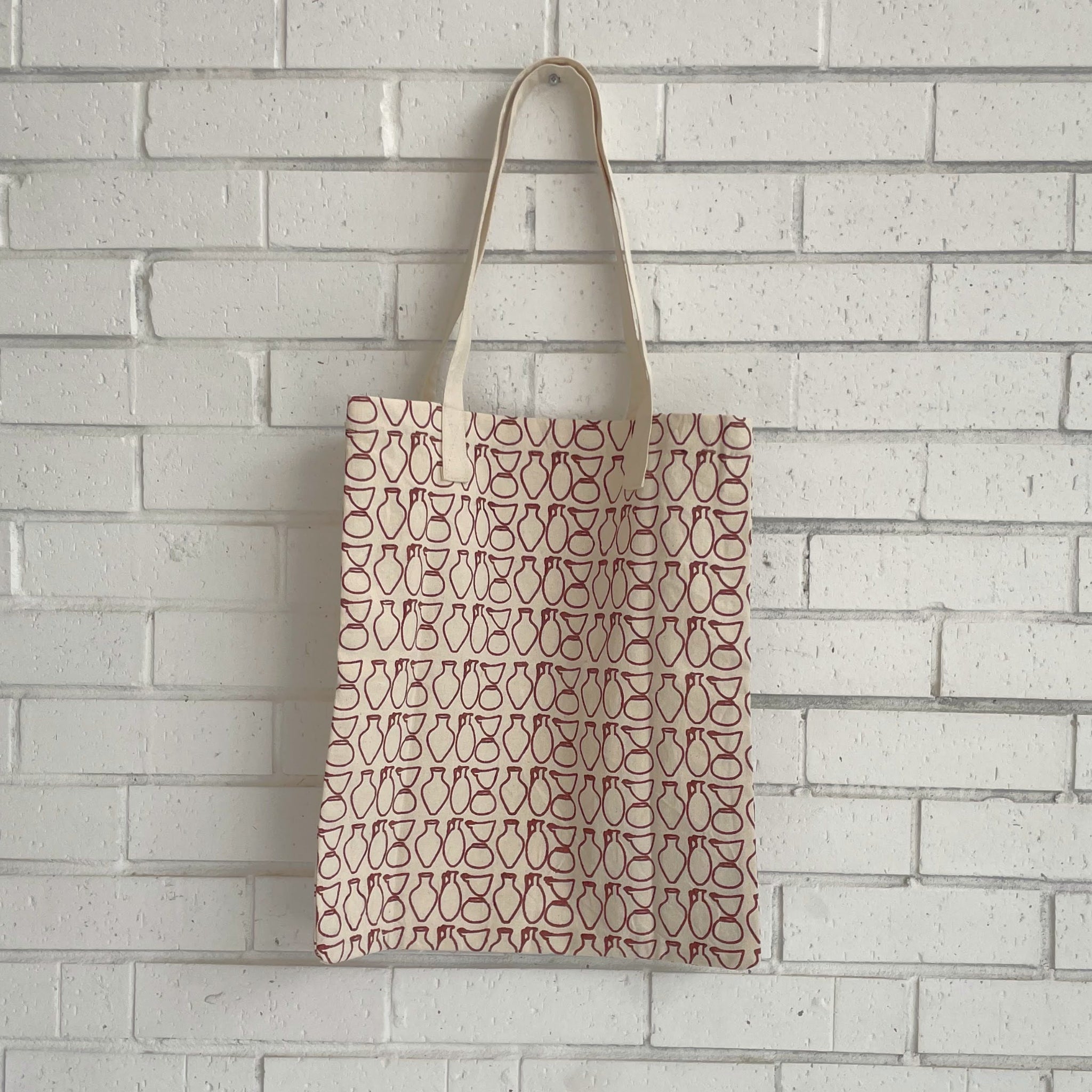 Tote bag with a pottery pattern hanging against a white brick wall.