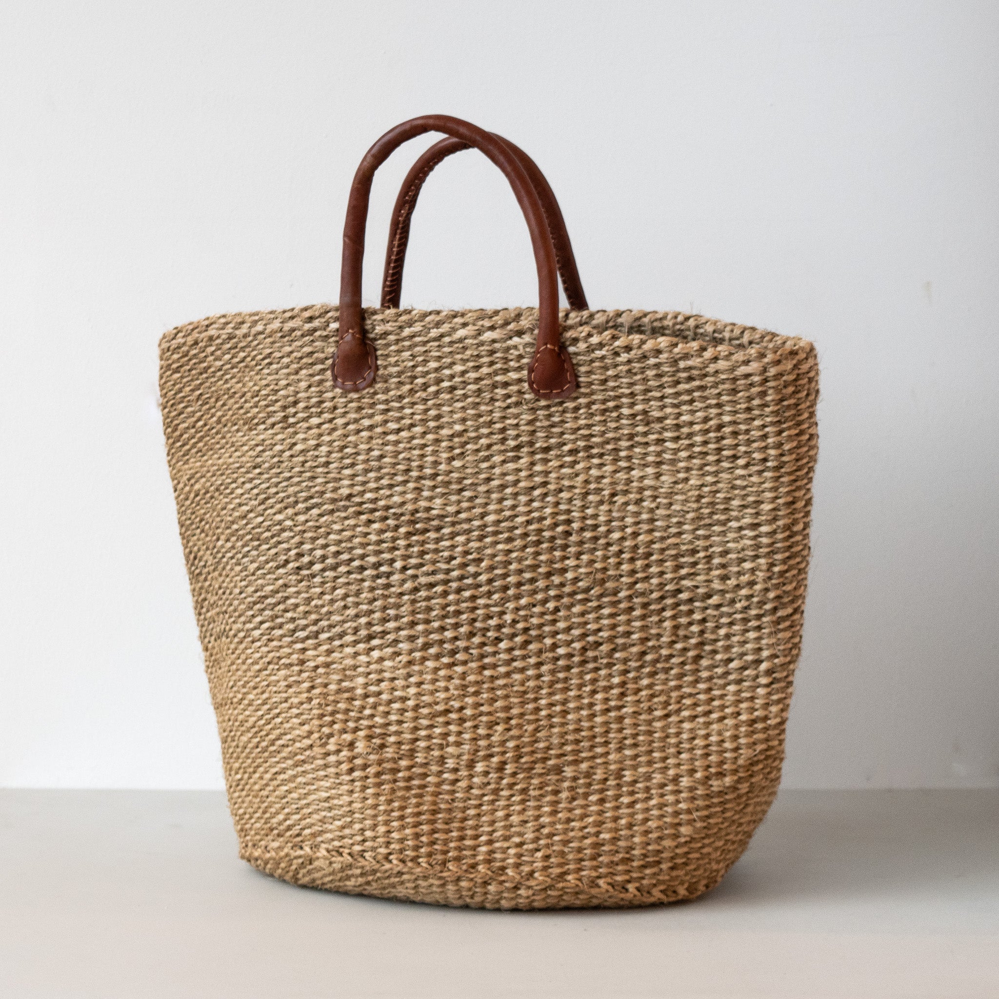 A sisal woven bag with leather handles, featuring a striped pattern with colors beige, black, and brown.