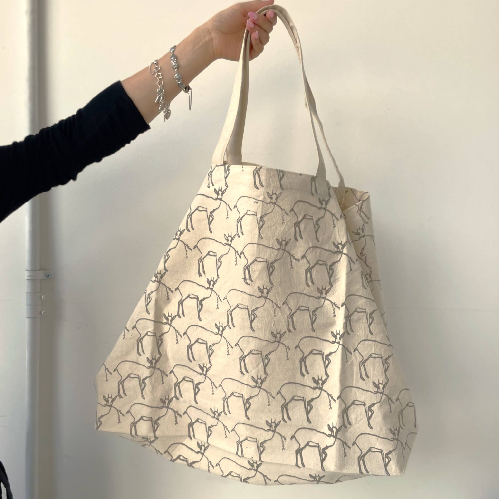 Beige tote bag with animal pattern held by a hand against a plain background
