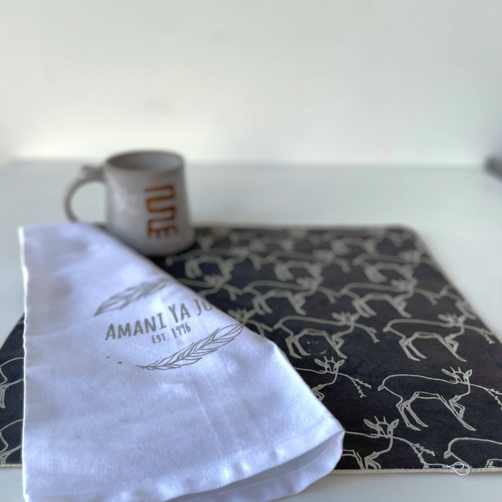 White napkin with text on a gray placemat with deer pattern, mug in the background