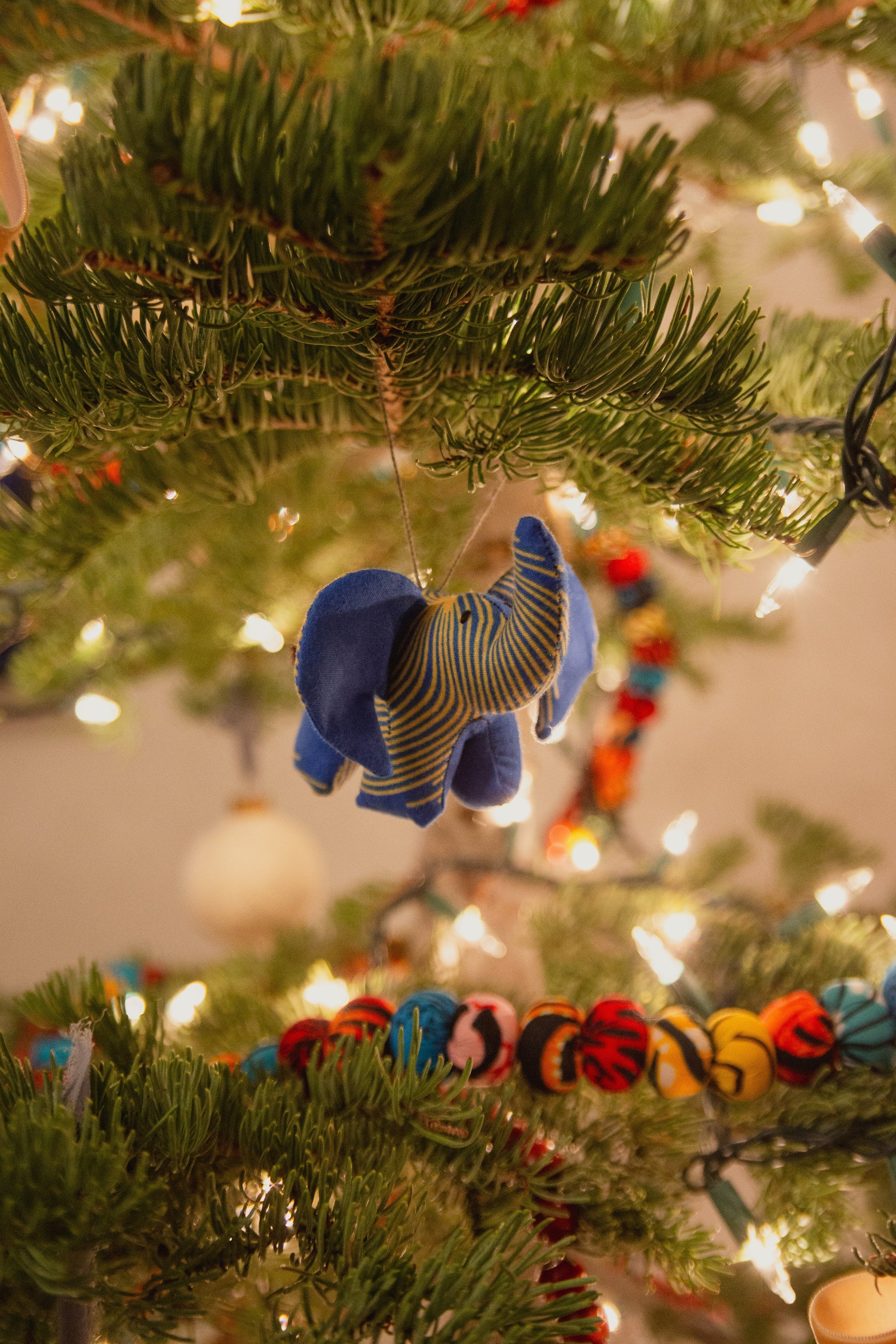 Blue elephant ornament hanging on a decorated Christmas tree with lights.