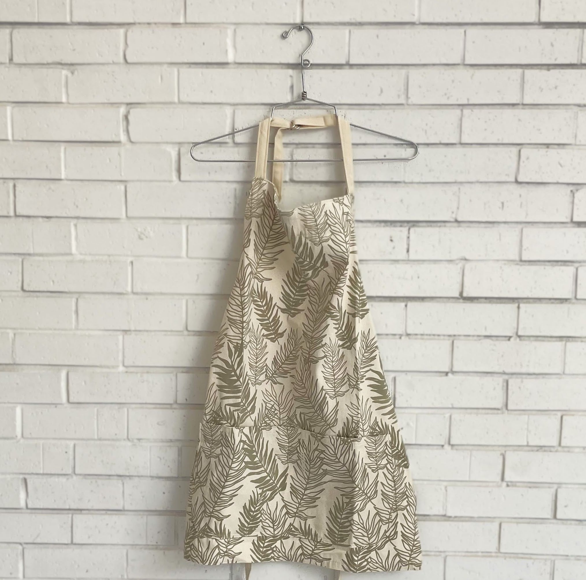 Fern-patterned apron on a hanger against a light brick wall