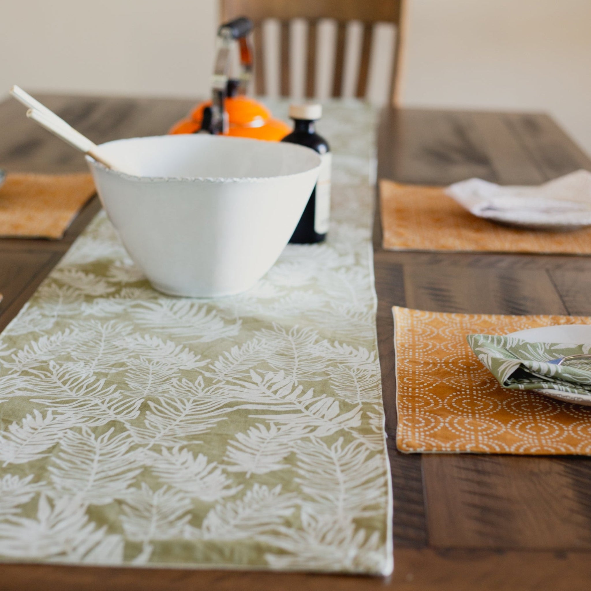 Dining table setting with a white bowl, patterned placemats, table runner, and napkins.