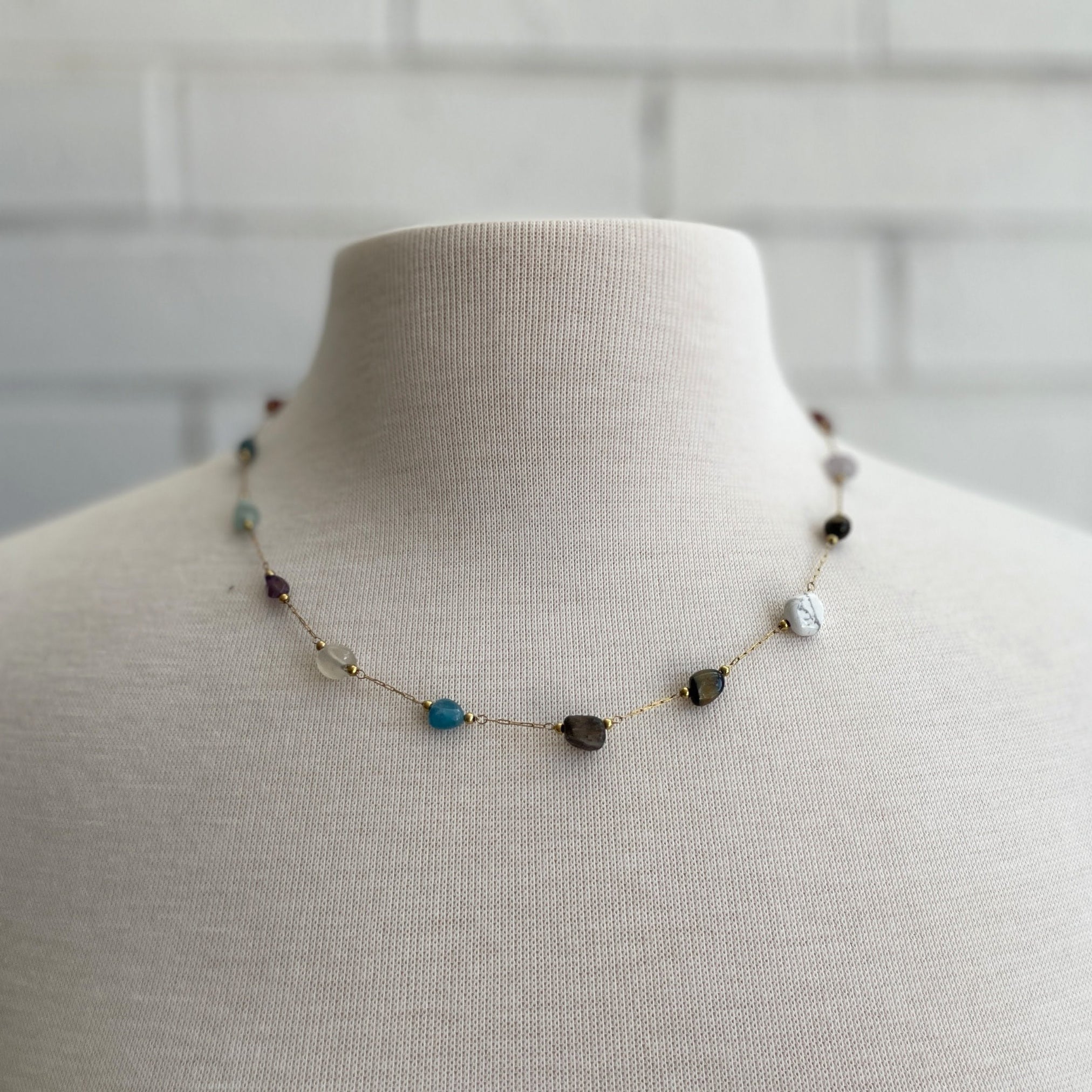 Necklace with multicolored stones on a mannequin against a tiled wall background