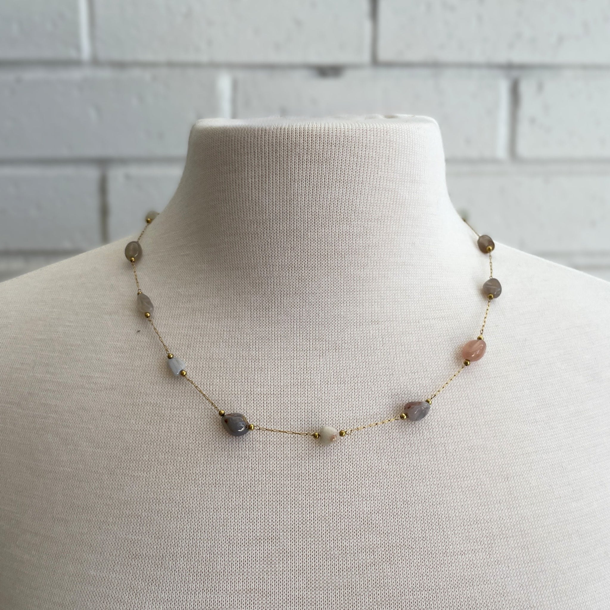 Necklace with stones on a mannequin against a gray tiled wall