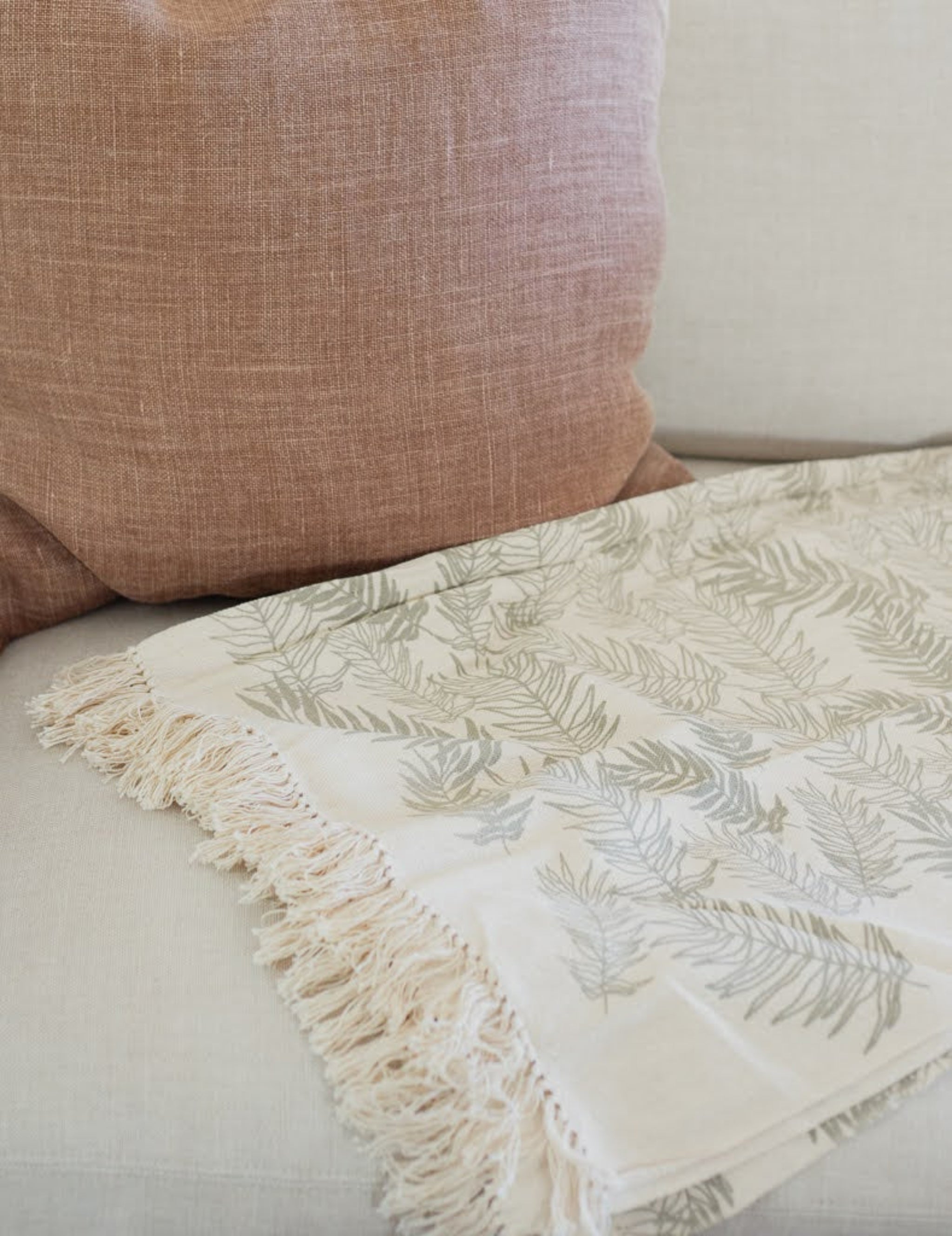 Handwoven cream throw with fern leaf pattern and tassels on a couch