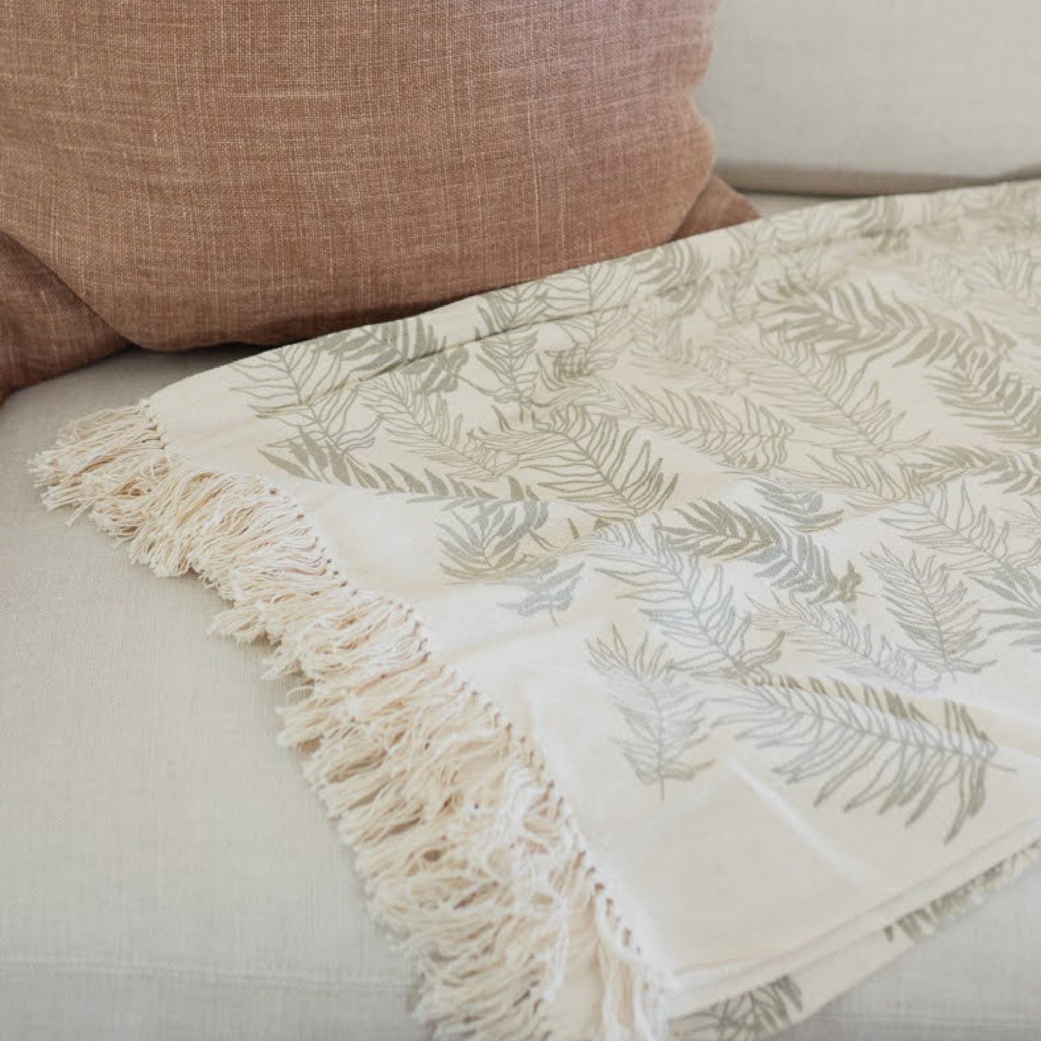 Handwoven cream throw with fern leaf pattern and tassels on a couch