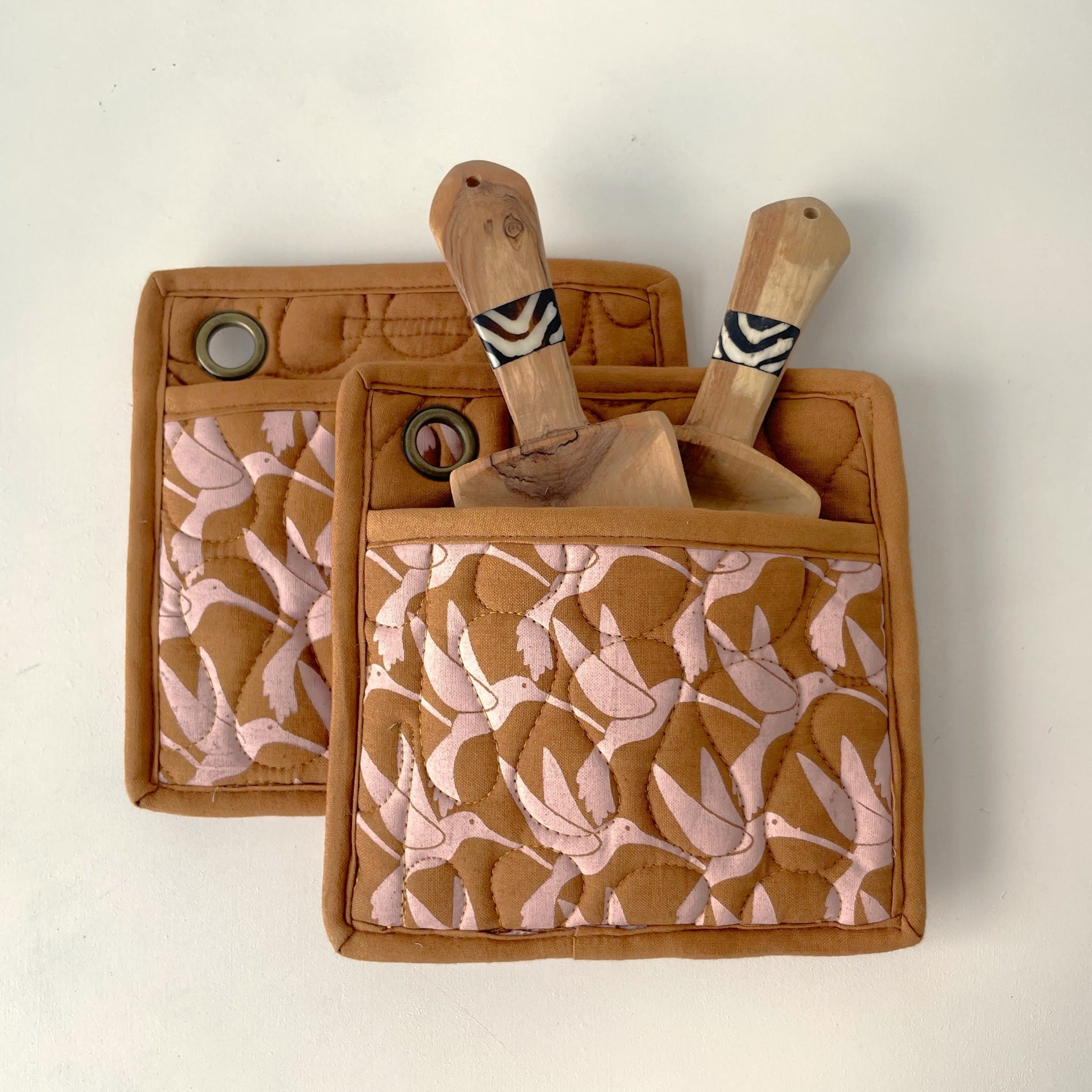 Set of wooden utensils in a brown patterned pot holder on a light background