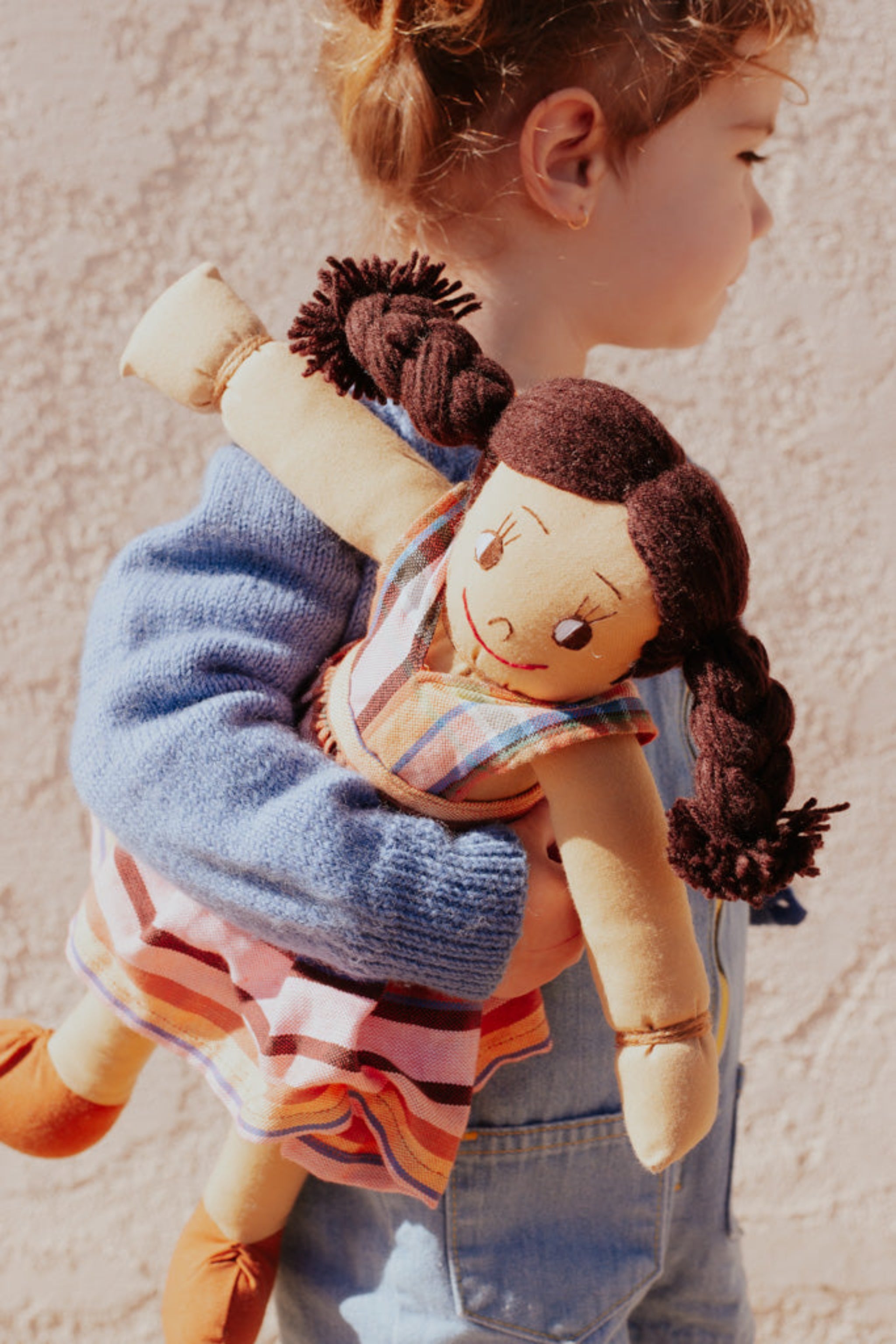 A child holding a brown doll with yarn hair, dressed in a striped kikoy outfit.
