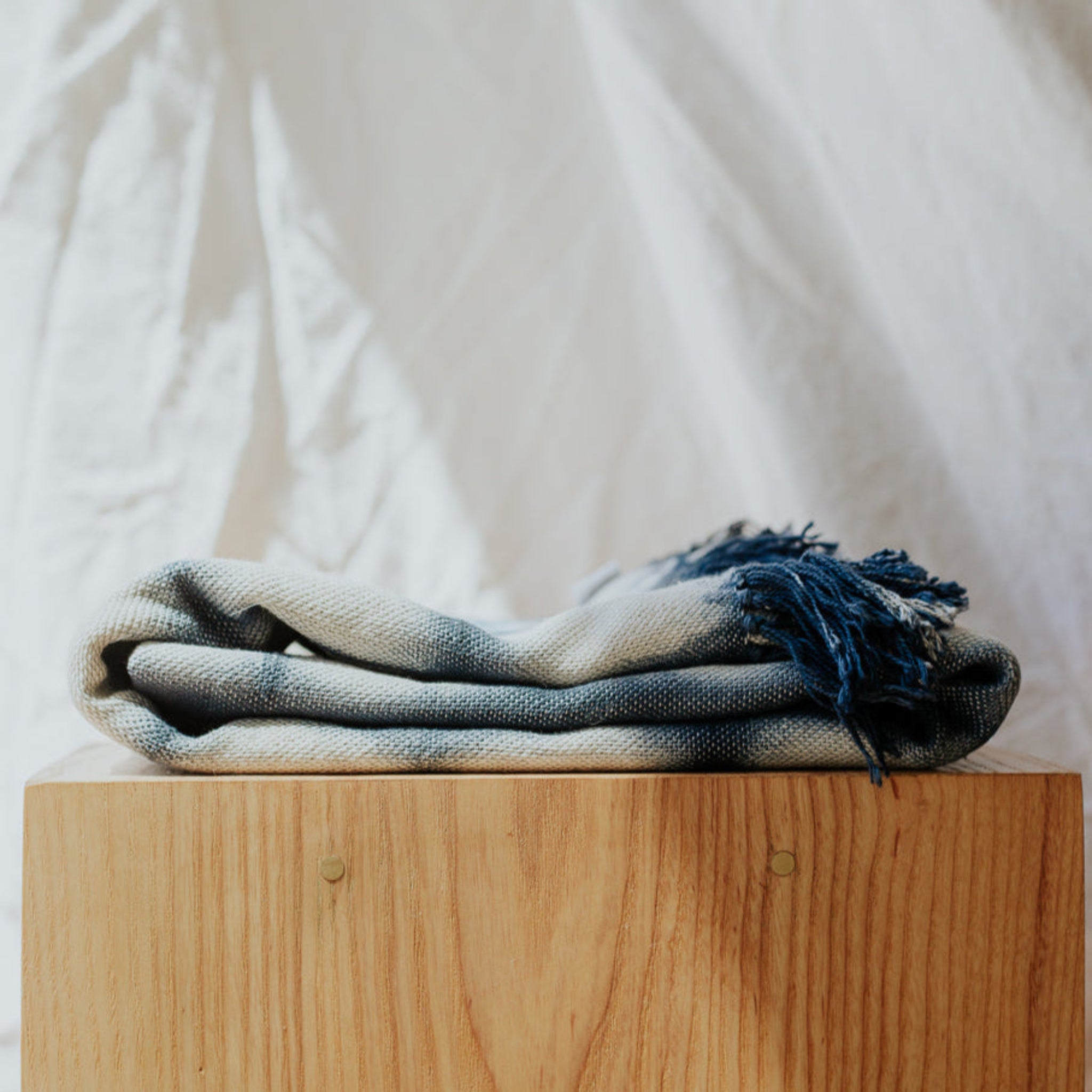 Blanket with fringes on a wooden block against a white curtain background
