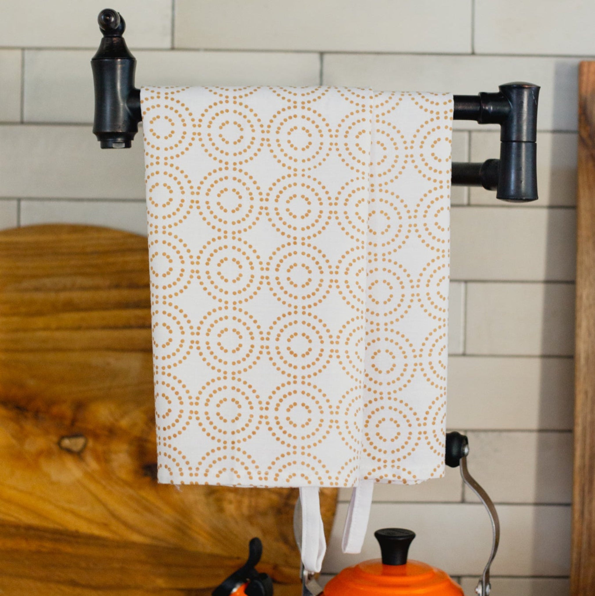 Patterned towel hanging on a towel rack with an orange kettle below in a kitchen setting.