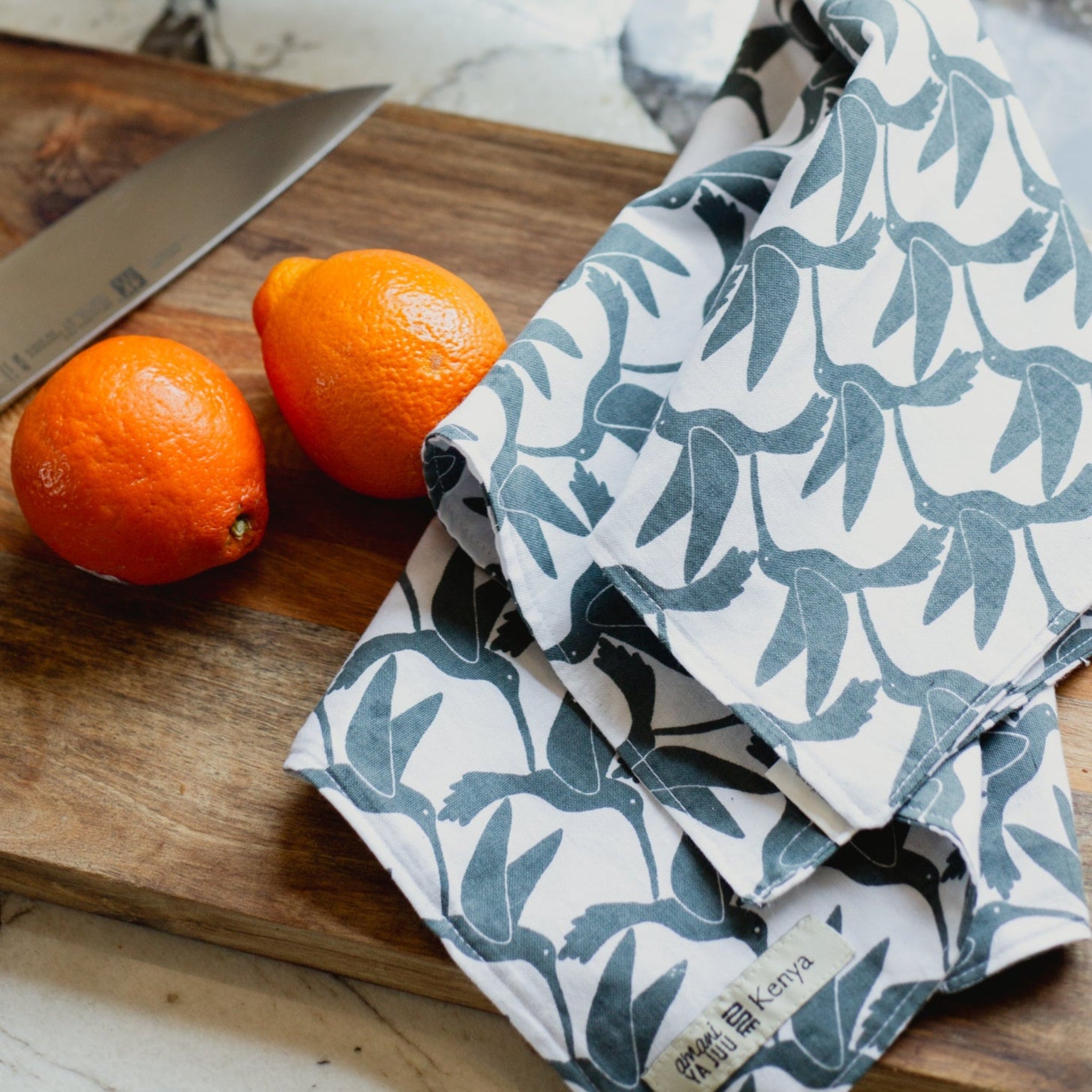 Folded patterned cloth on a wooden cutting board with oranges and a knife.