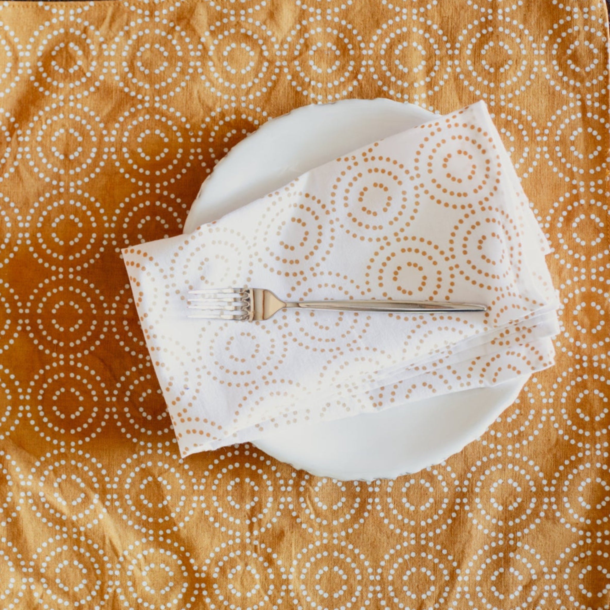 White plate with folded white napkin and silver fork on a patterned orange tablecloth