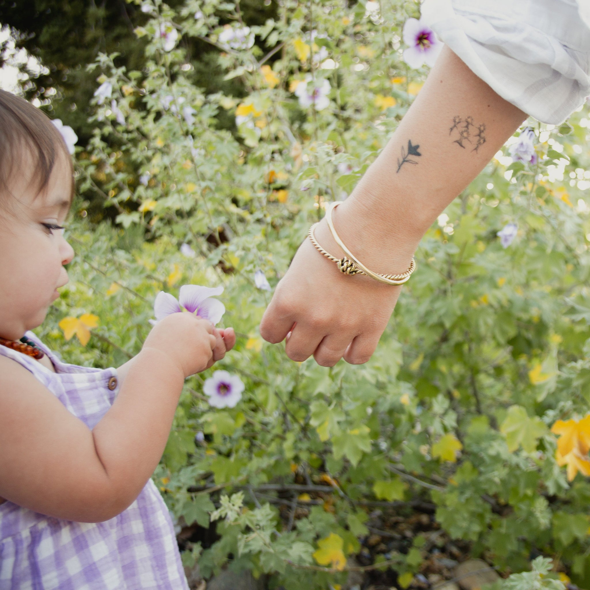 Child holding a flower with an adult's hand in a garden setting