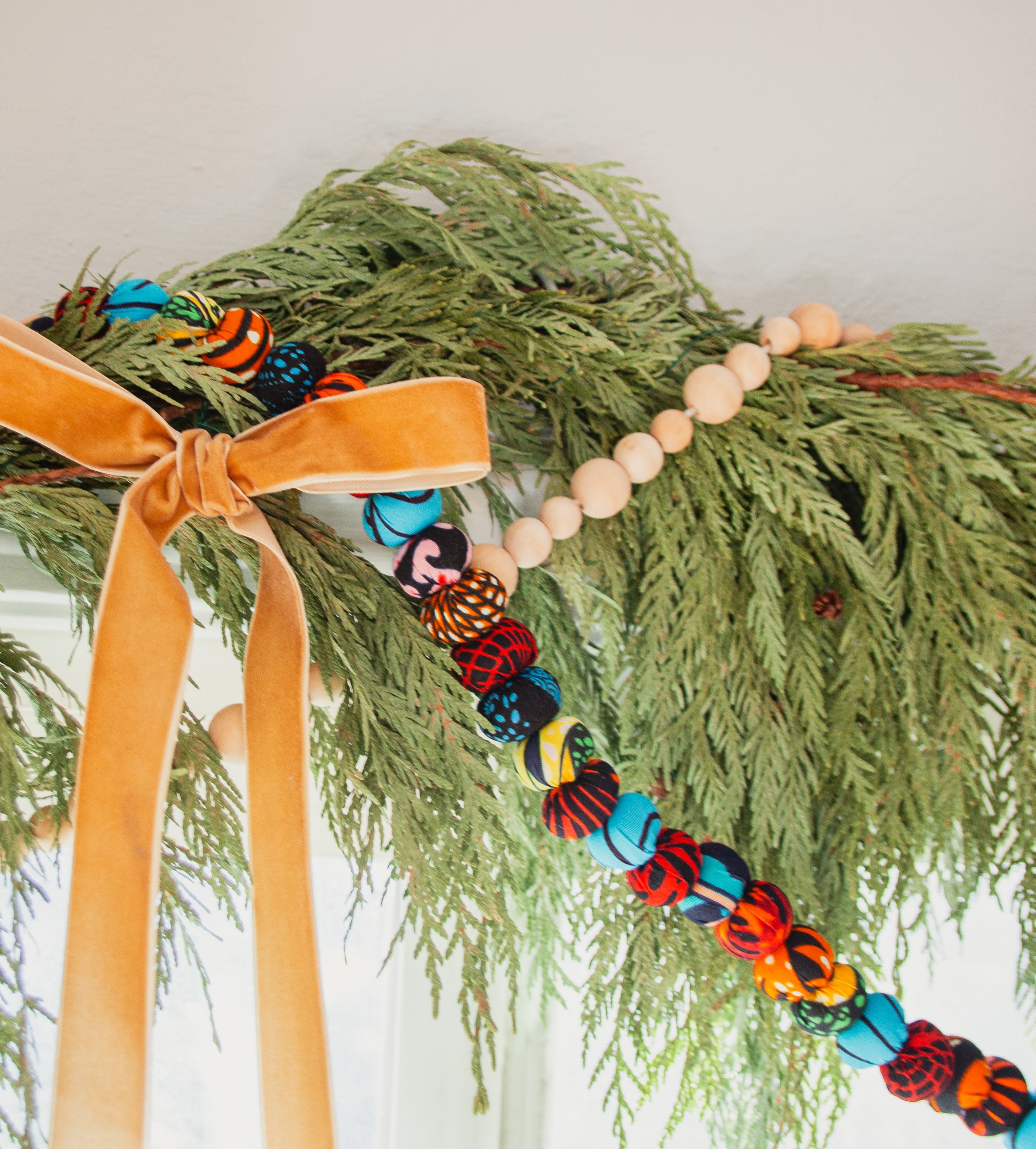 Decorative garland with colorful beads and a yellow ribbon on green foliage.
