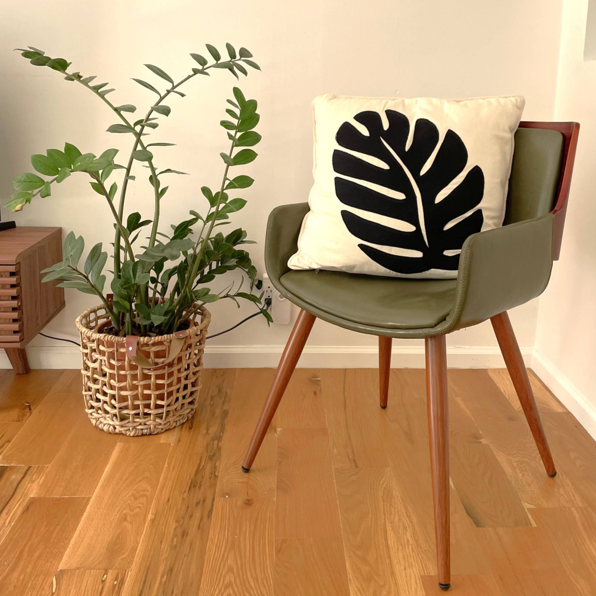Green chair with a leaf-patterned pillow next to a potted plant on a wooden floor.