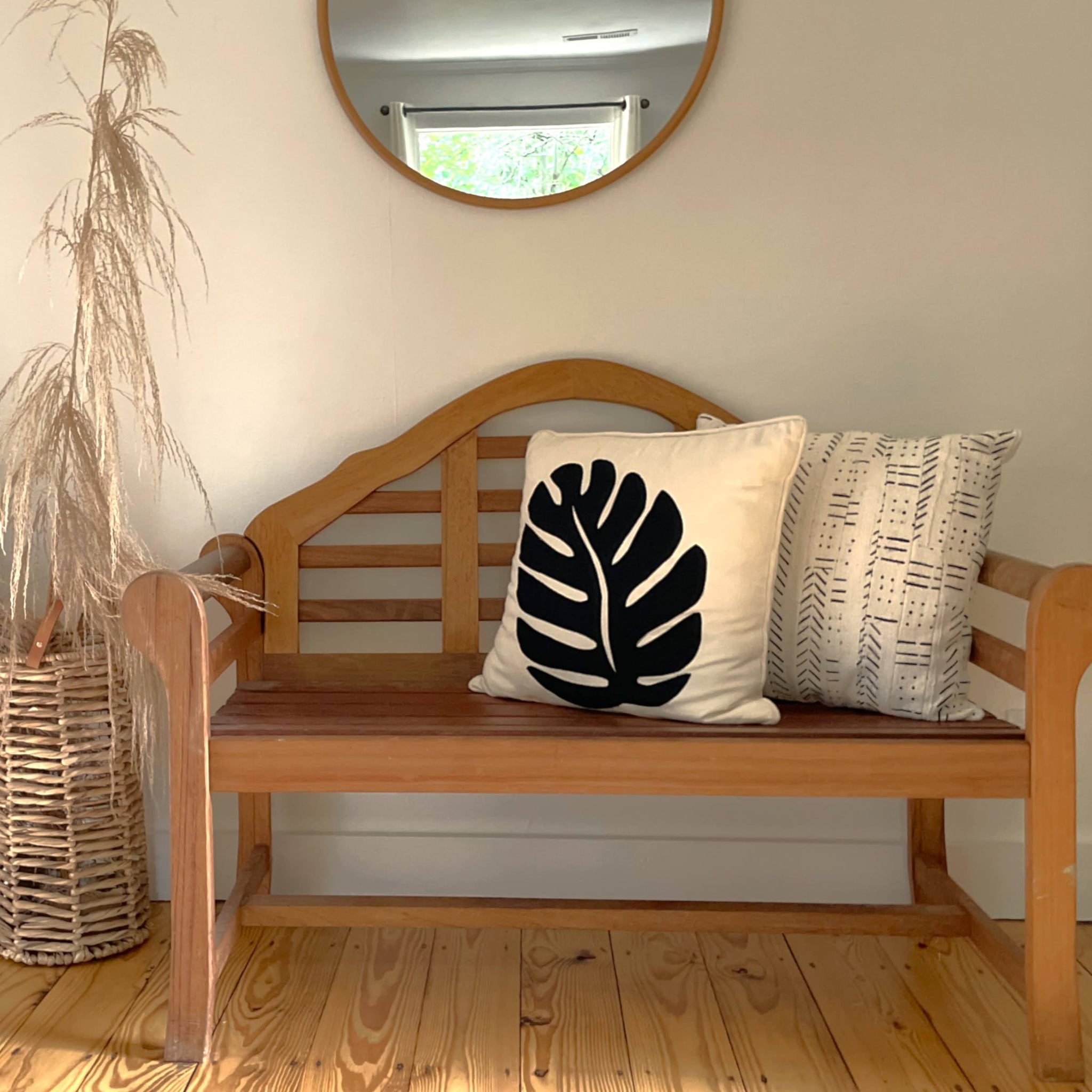 Wooden bench with decorative pillows in a room with a mirror and plant.