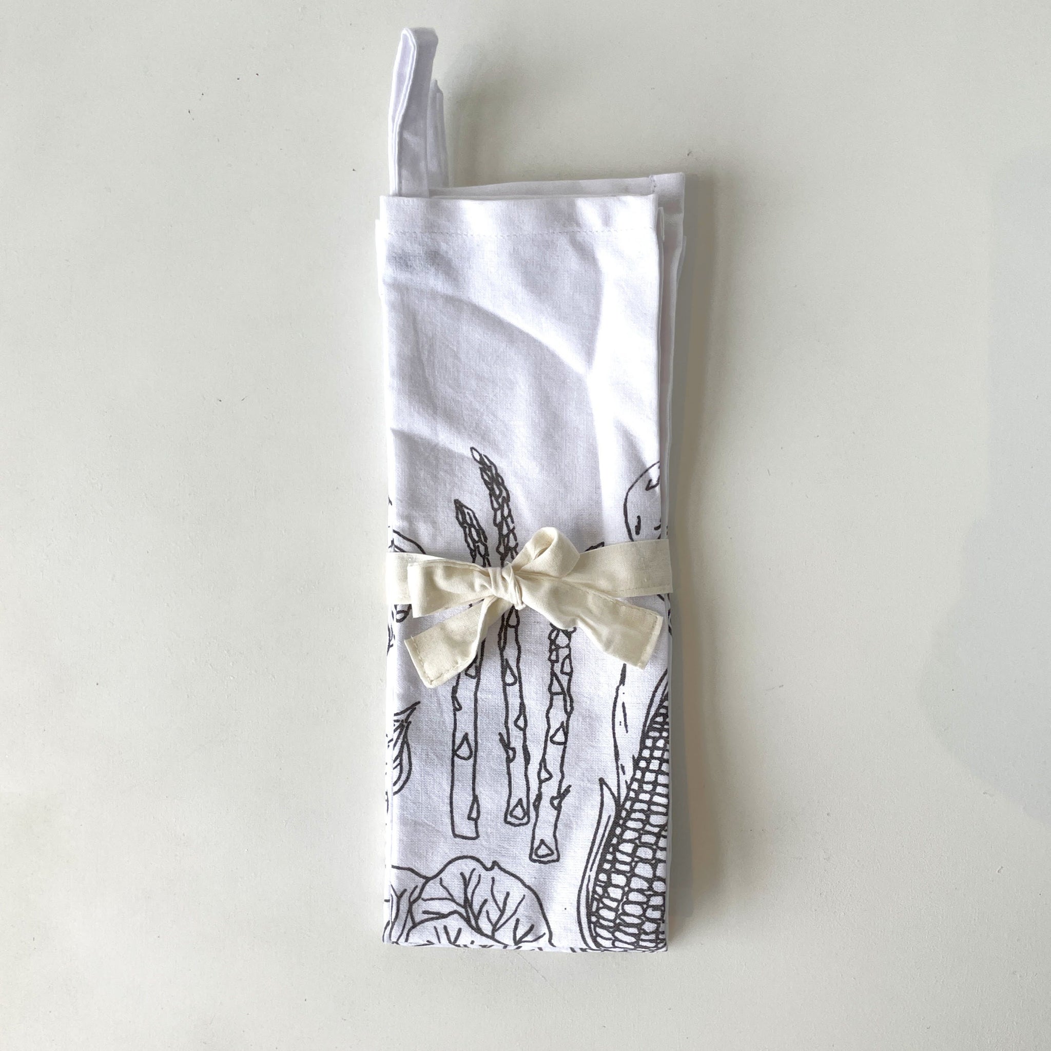 Folded fabric dish towels with vegetable pattern and white bow on a light gray background