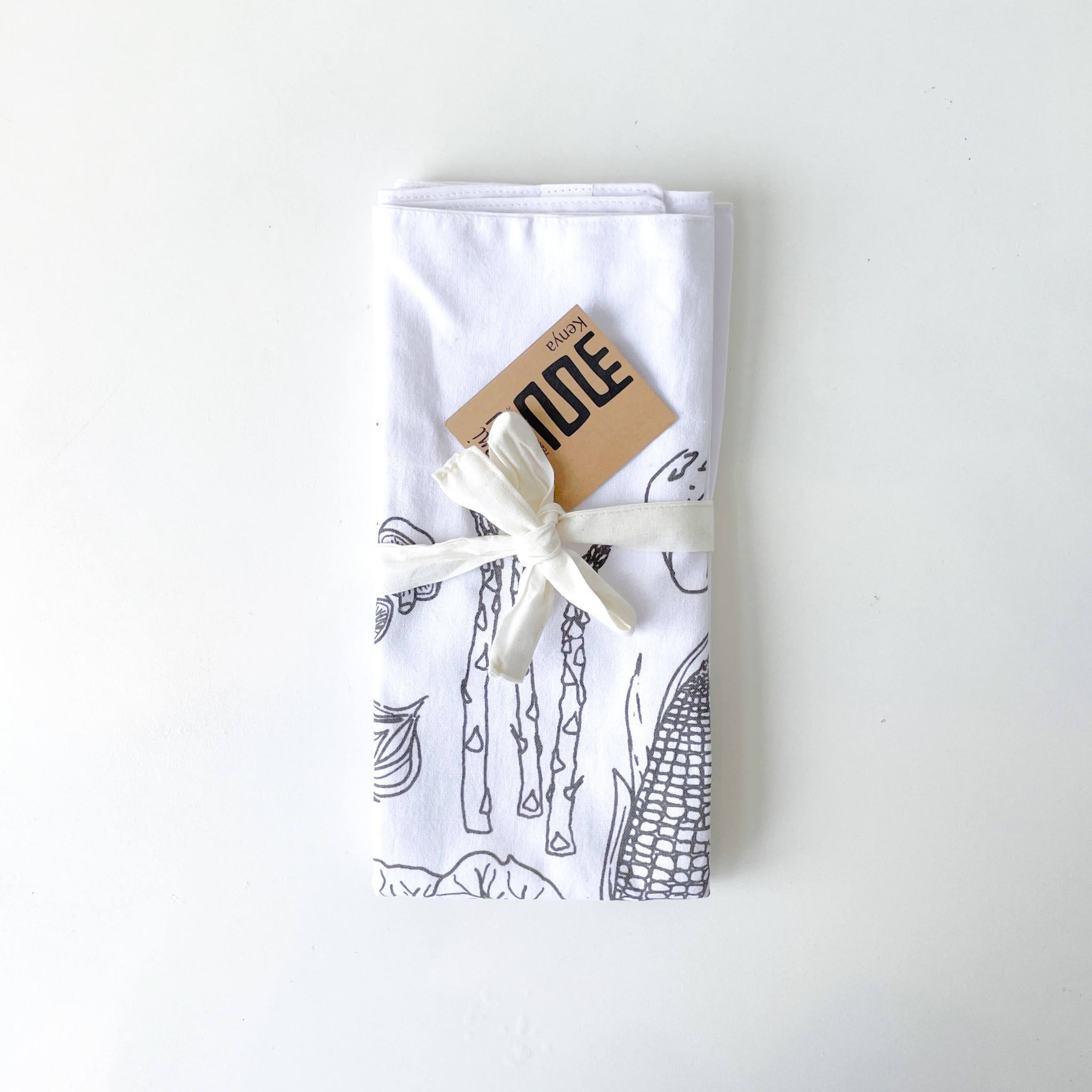 Folded white towel with mocha vegetable prints and a white bow on a white background