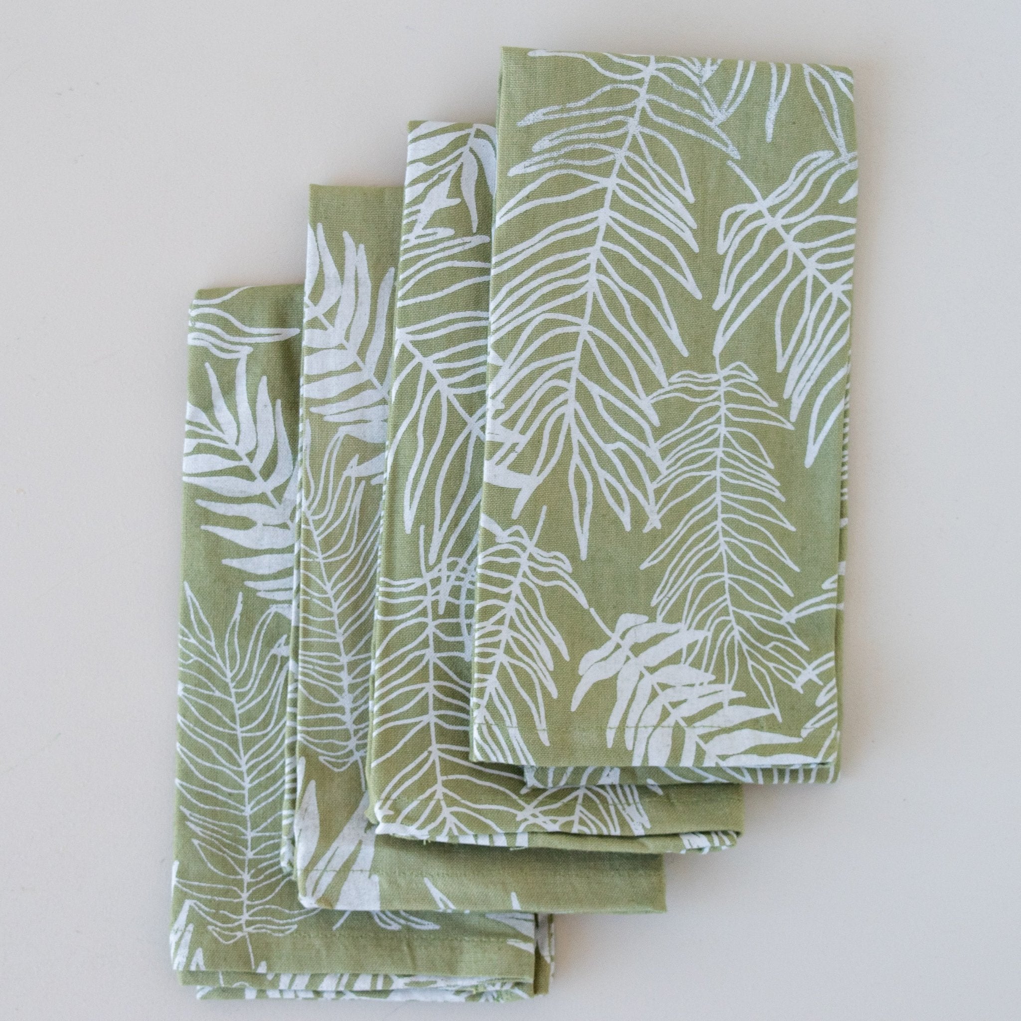 A set of four green cotton napkins with a white leaf pattern, displayed on a neutral background.
