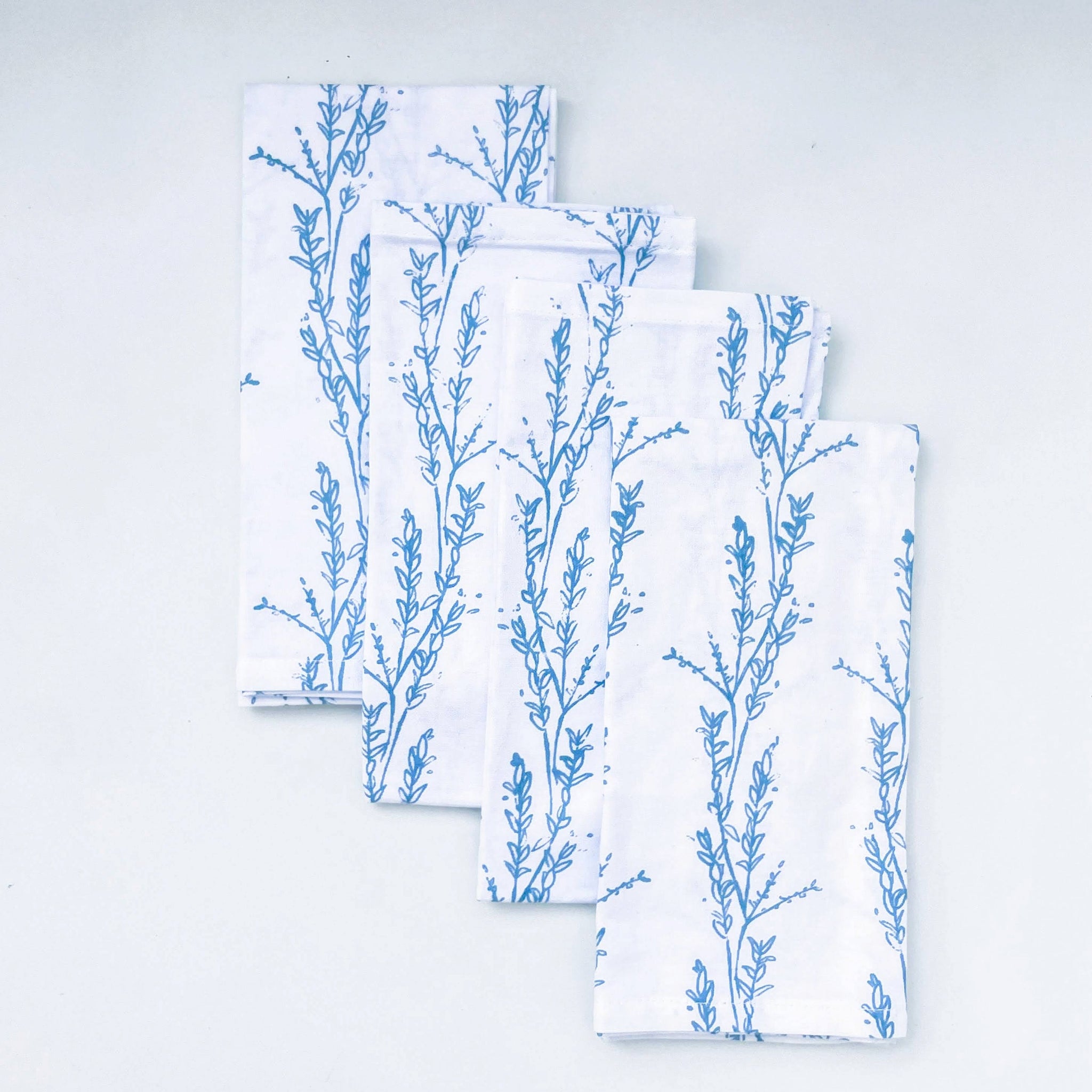 Set of folded white napkins with blue floral patterns on a light gray background. Screen Print Napkin Set - Kenyan materials and design for a fair trade social enterprise