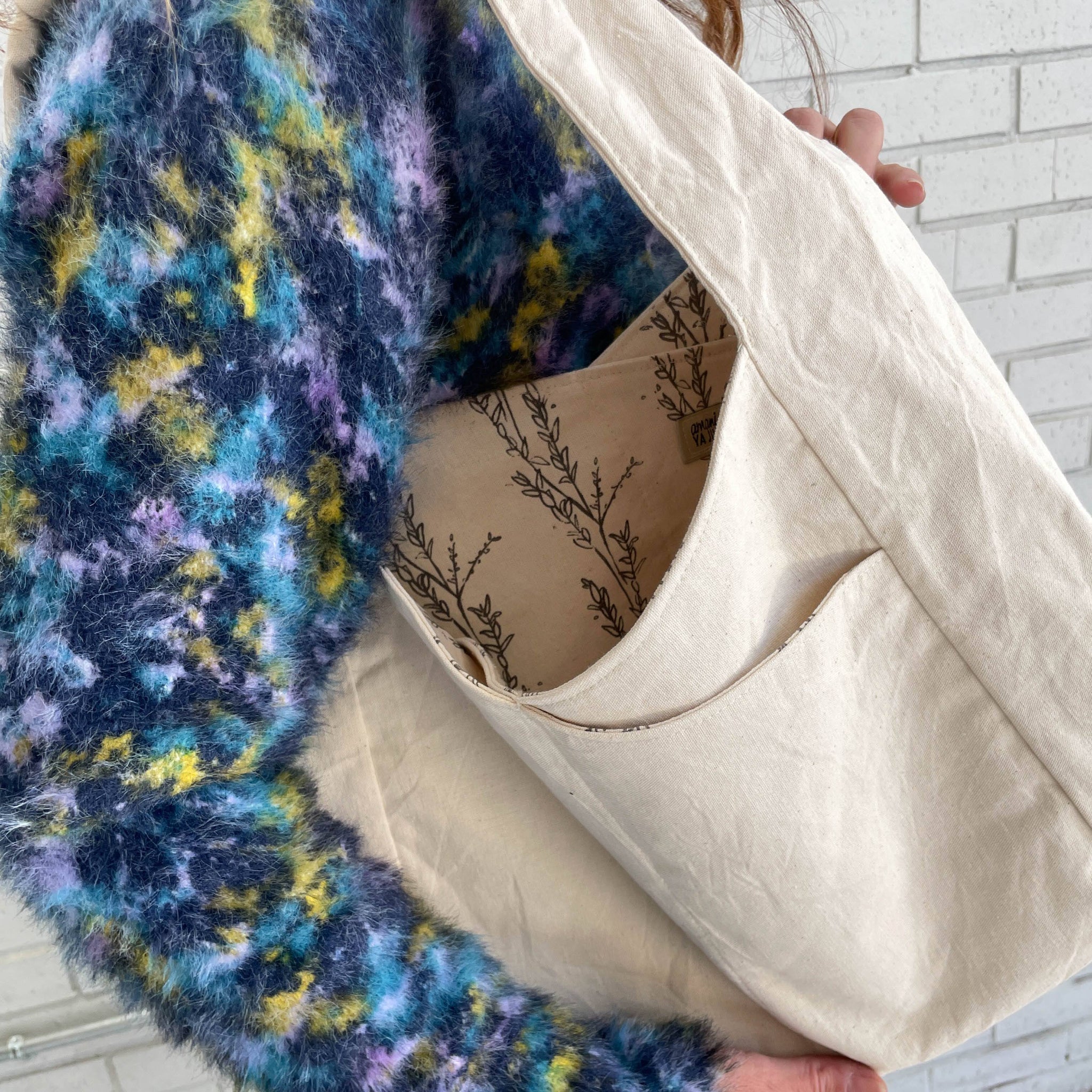 Close-up of a textured colored sweater and a floral patterned and white fabric shoulder bag.