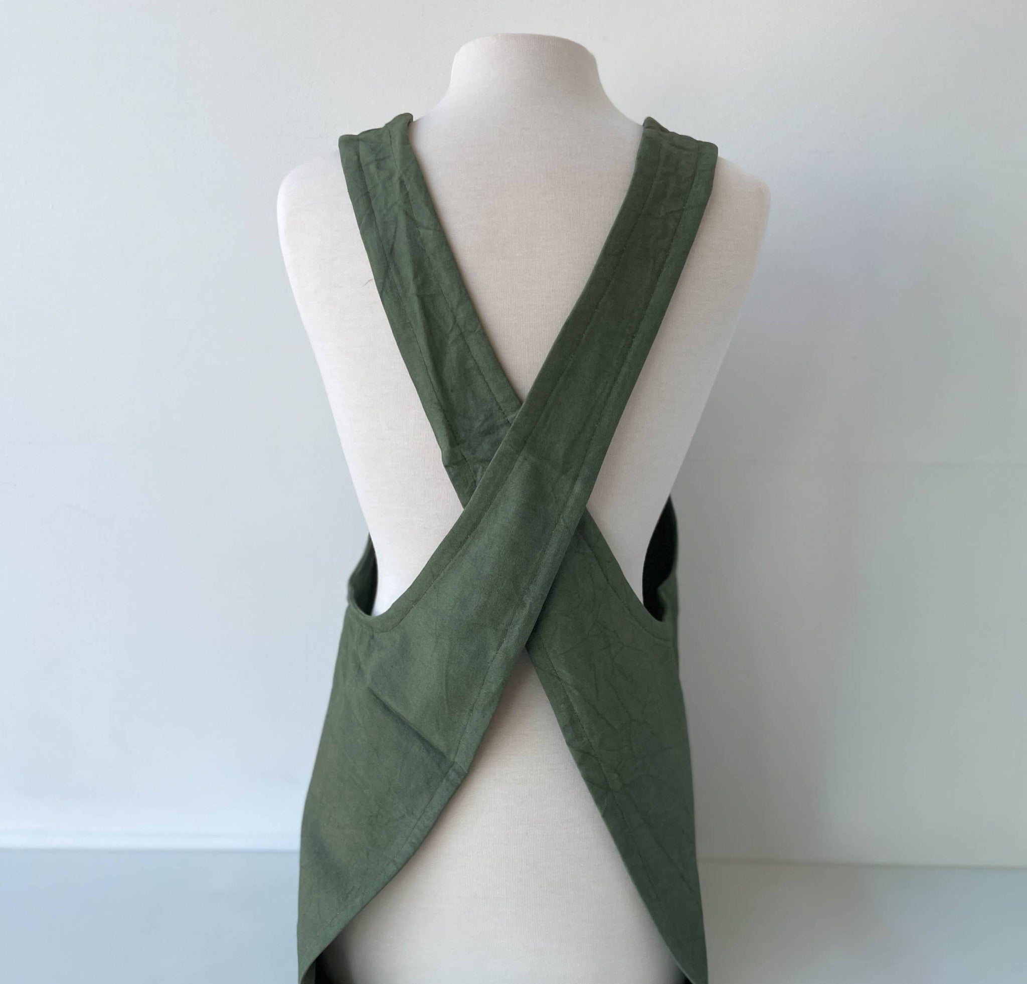 Green apron with criss-cross design on a mannequin against a plain background