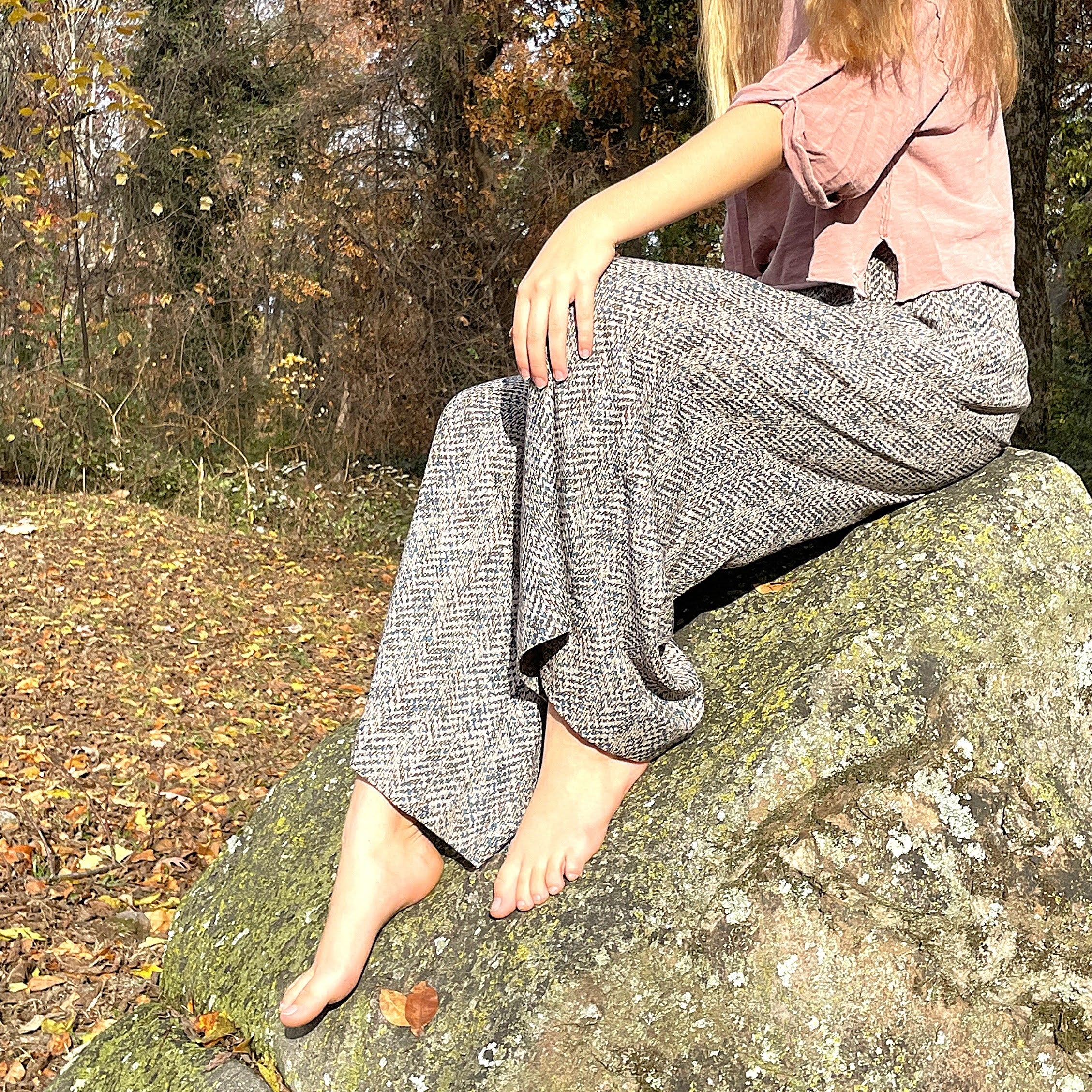 Person sitting on a rock in a forest wearing gray pants and a pink shirt.