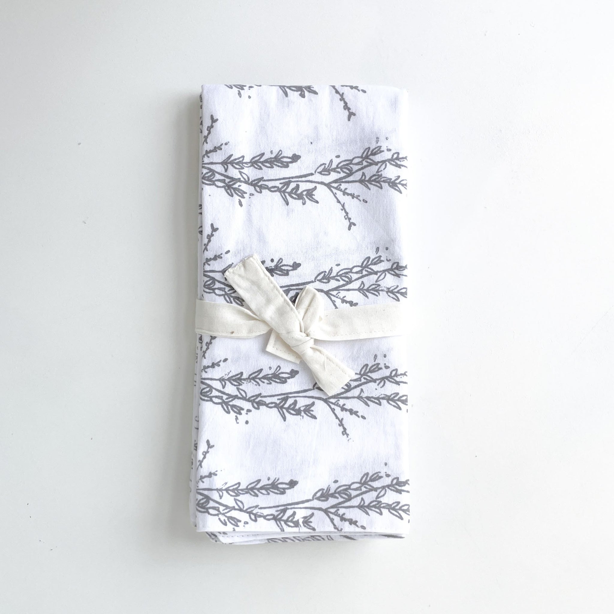 Folded fabric tea towels with gray leaf pattern and white bow on a light gray background