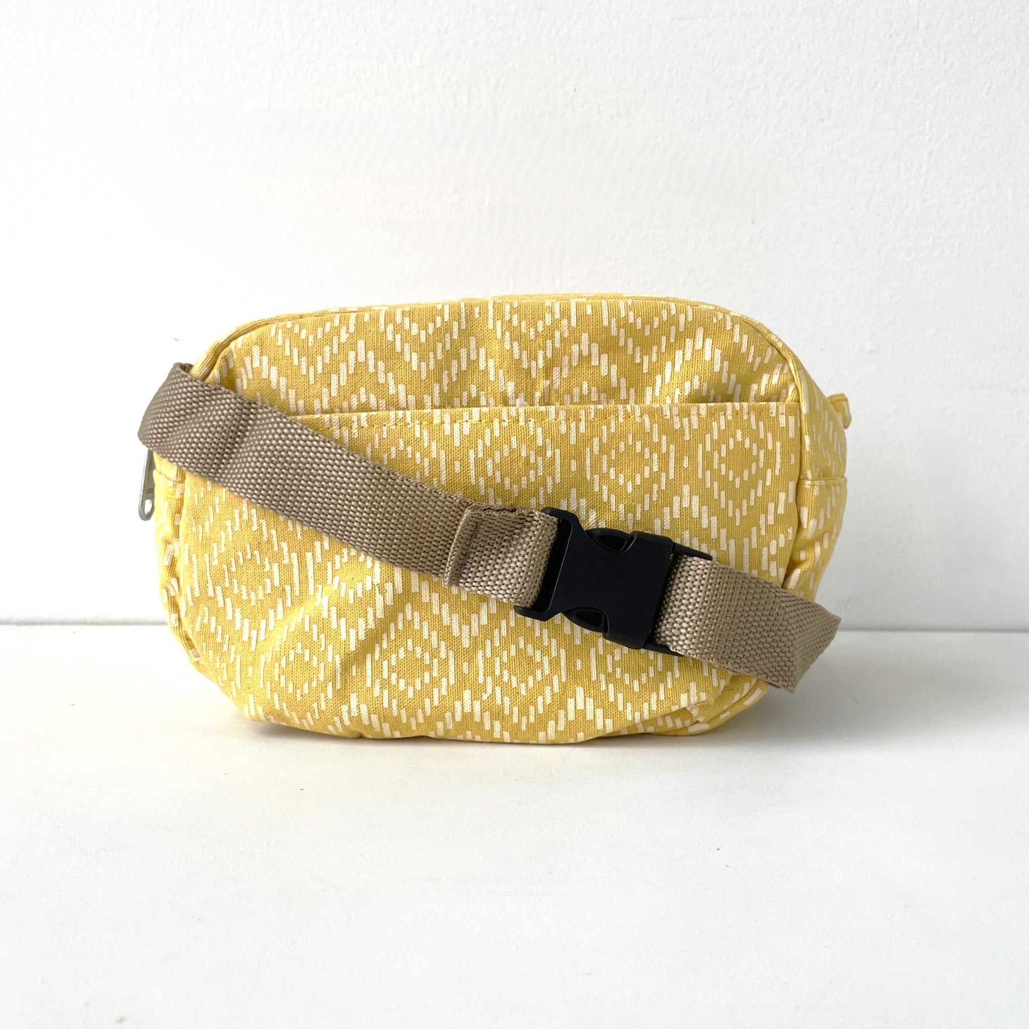 Yellow patterned waist bag with a beige strap on a white background