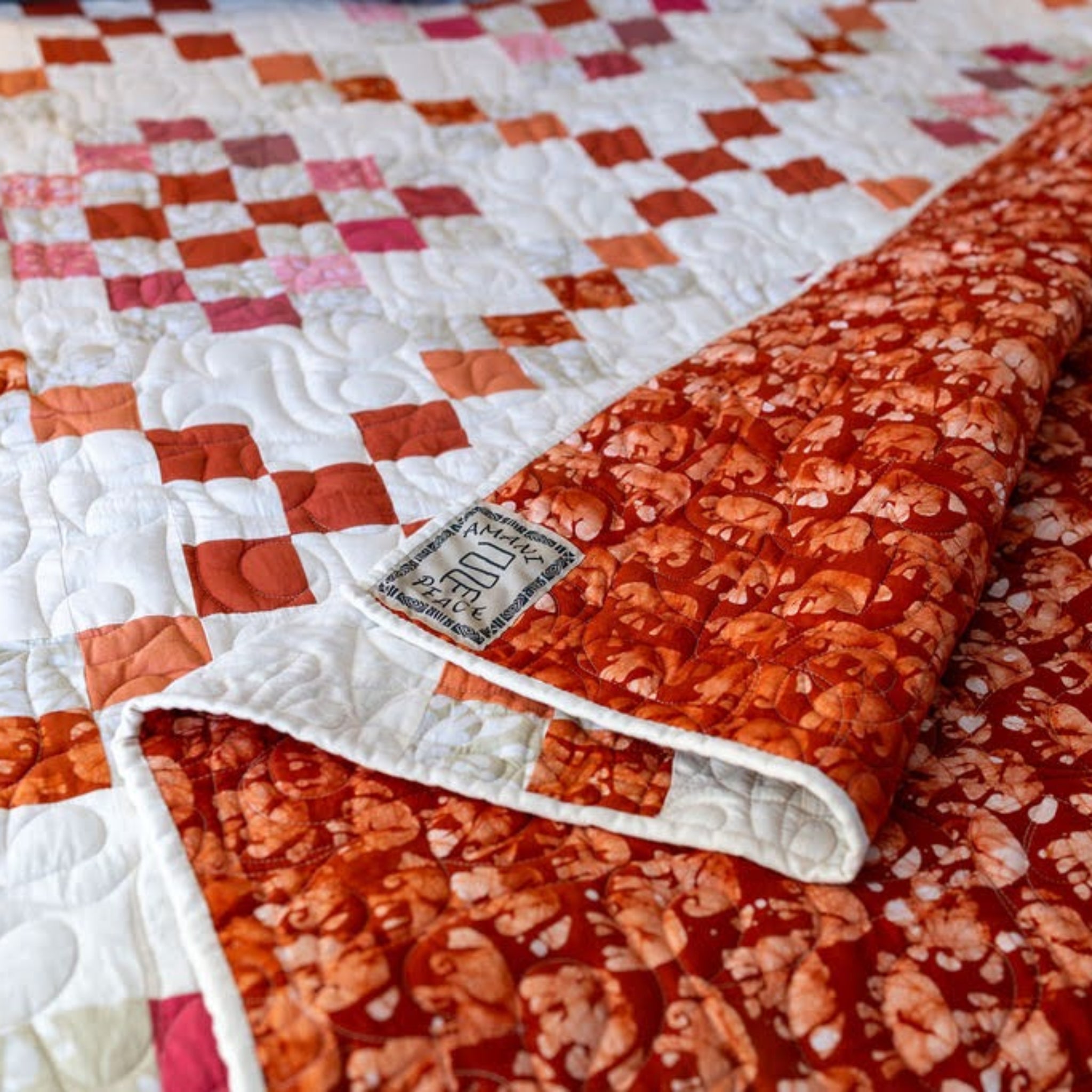 Detail of a diamond patterned quilt in red, orange, and pink showing the backing in a red elephant pattern.