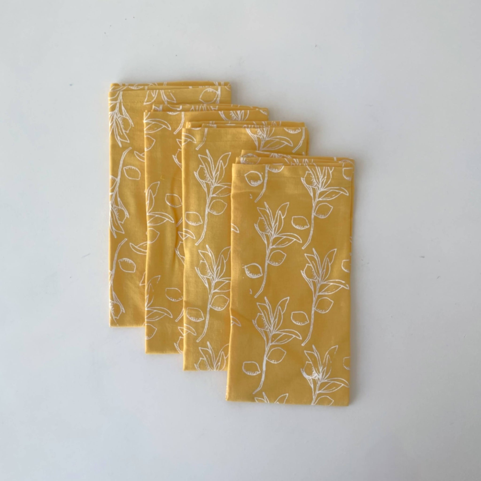 Set of four yellow fabric napkins with white citrus sprig pattern on a light background