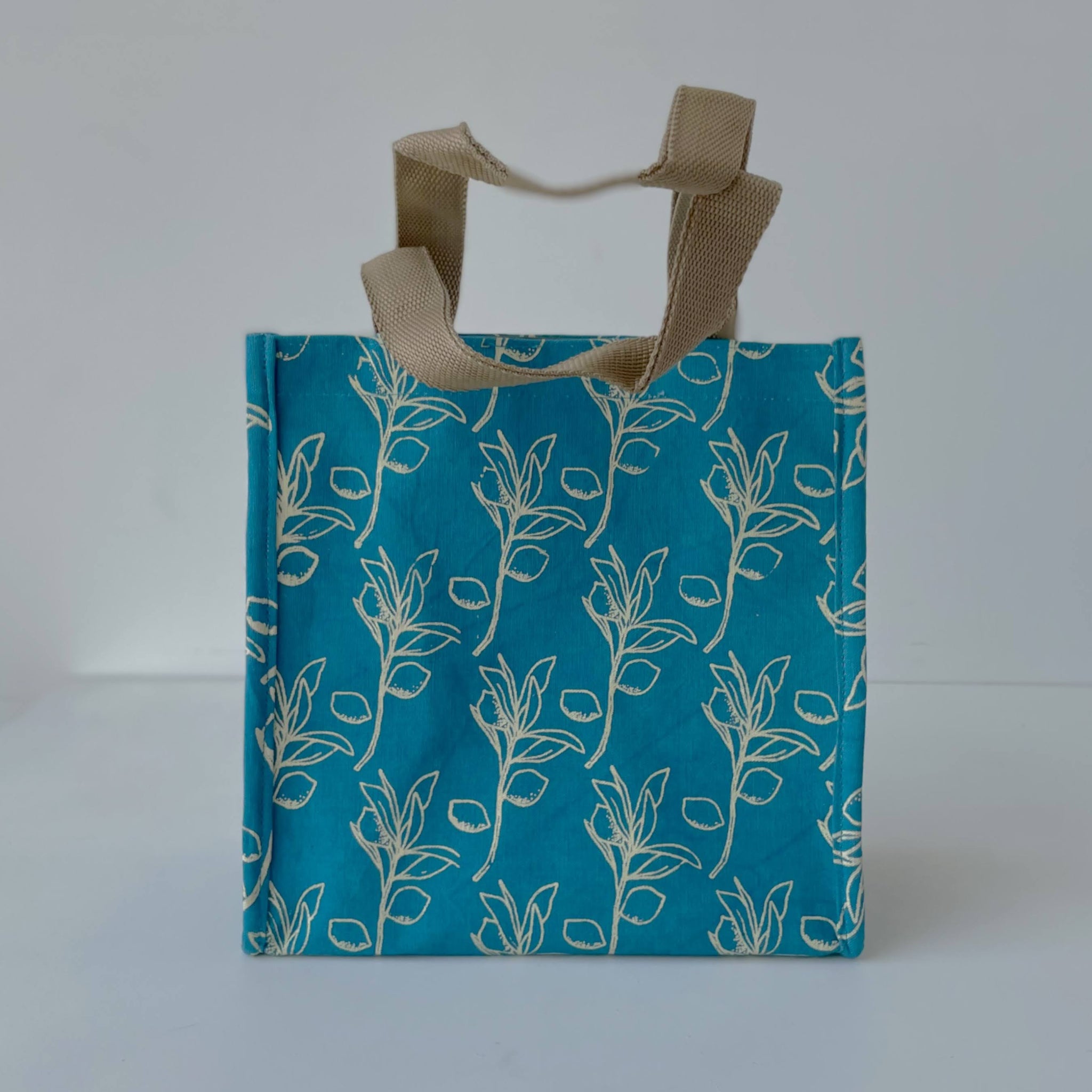 Blue tote bag with white citrus sprig pattern and brown handle on a white background