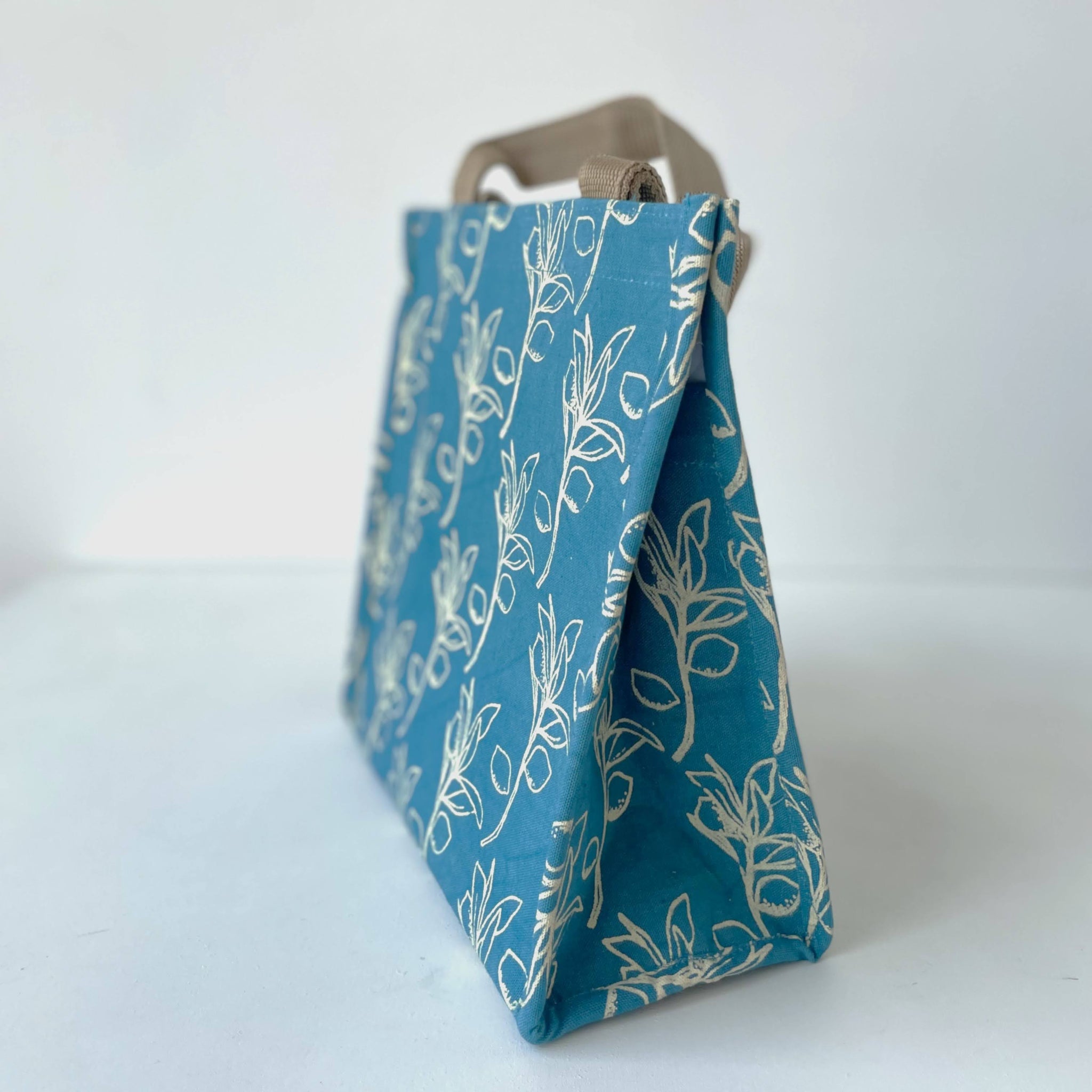 Blue fabric lunch bag with white citrus sprig pattern on a white background