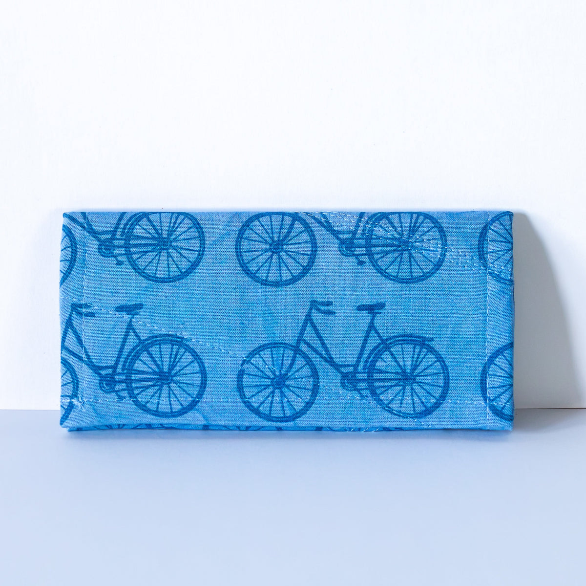 A small fabric zippered wallet in blue bike patterned material, shown flat against a light off-white background.