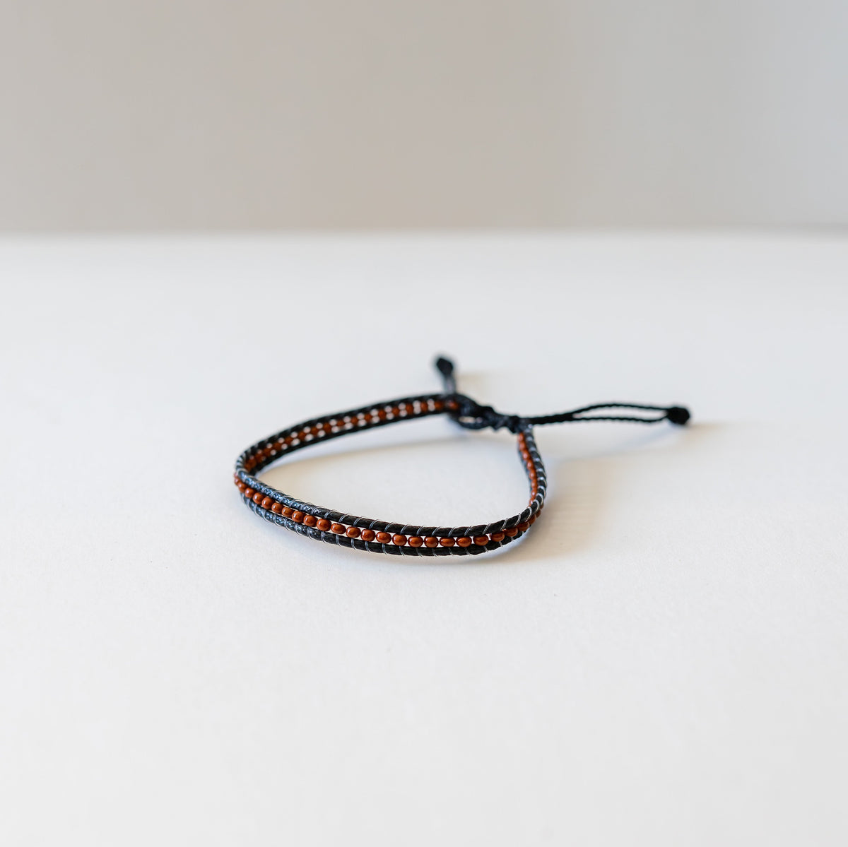 Adjustable dark brown bracelet with caramel-colored beads on a white surface