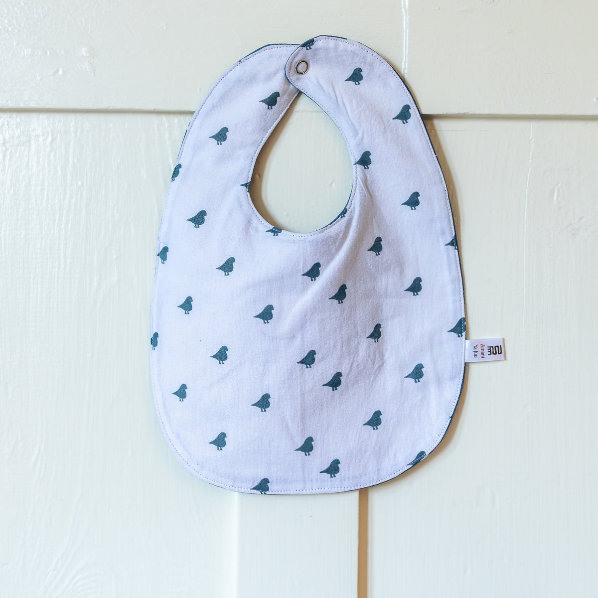 white baby bib with blue birds hanging on a white door
