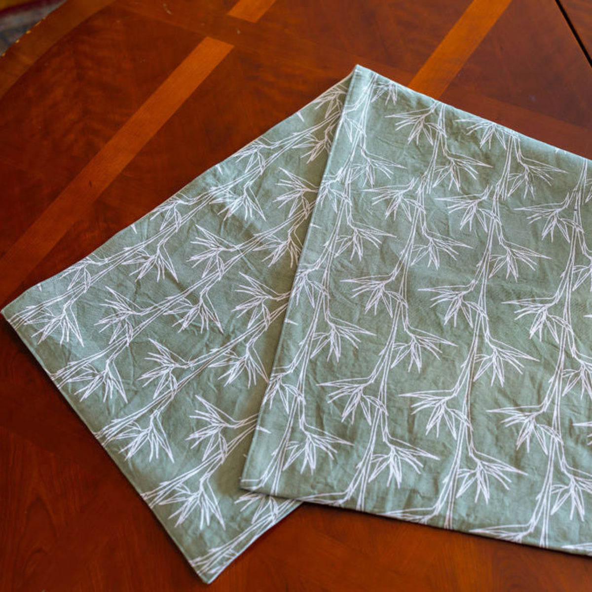 Sage green fabric table runner with a white bird of paradise pattern, displayed on a polished wooden table.