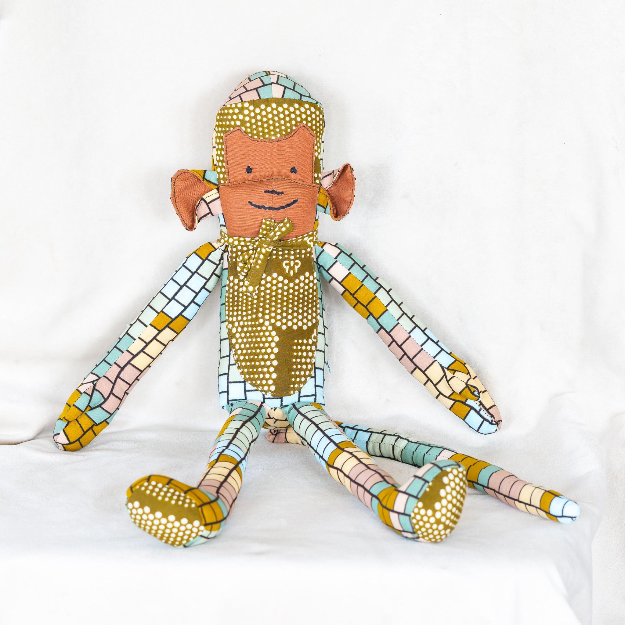 Stuffed monkey doll in greens and browns on a white surface